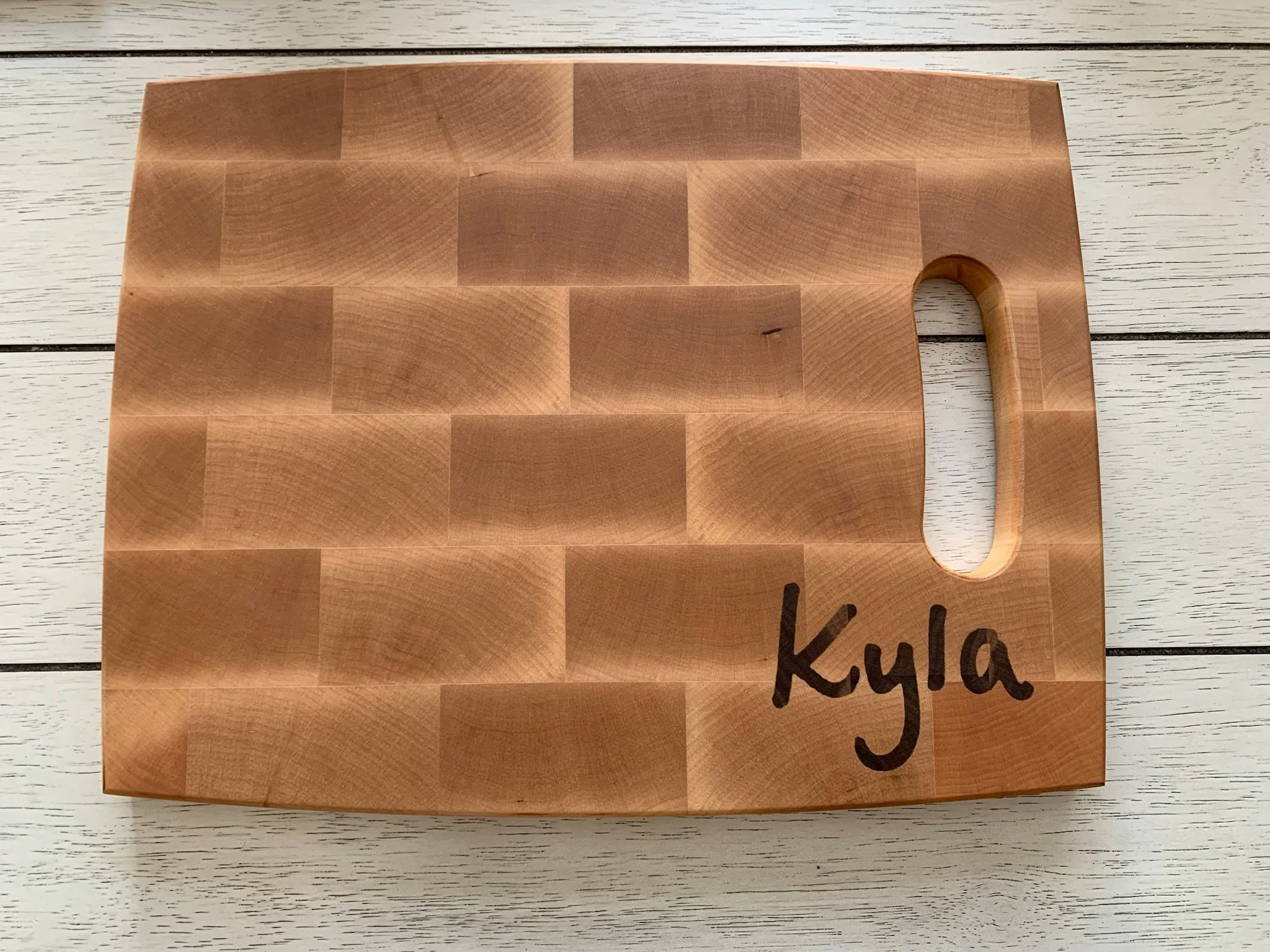 A wooden checking board on a white wooden surface with a partial view of handwritten text that says 'KYLA'.