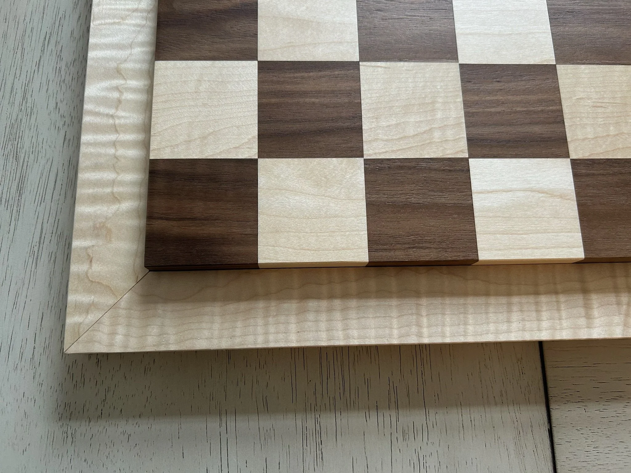 Close-up of a wooden chessboard with alternating light and dark squares placed on a white surface.