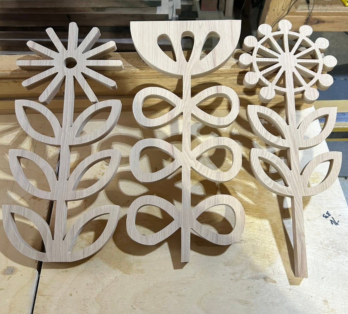 Three unfinished wooden snowflake decorations with intricate designs, placed on a wooden workbench.