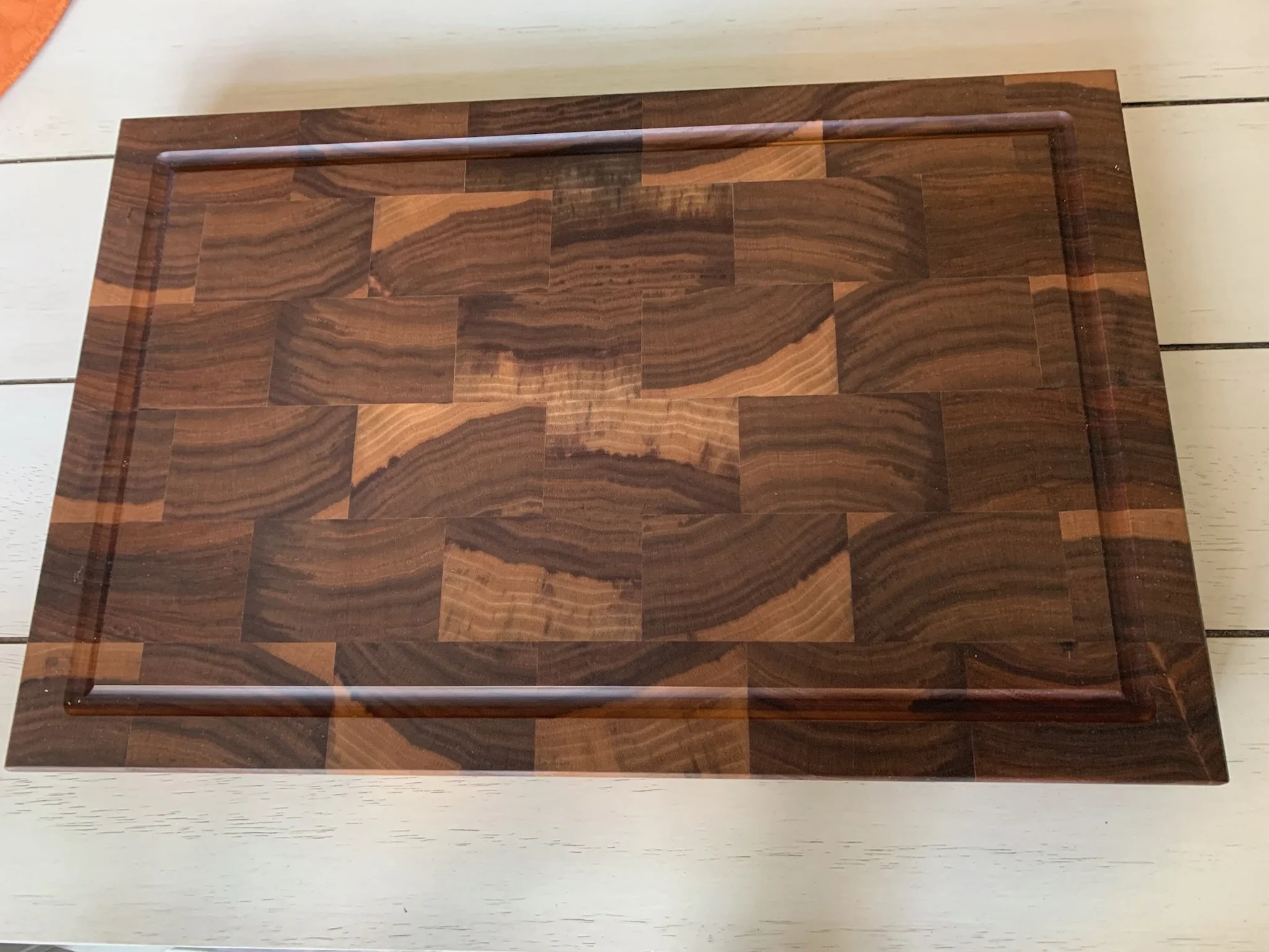 A rectangular tabletop with a woodgrain pattern, surrounded by a dark brown metal frame, placed on a light-colored wooden surface.