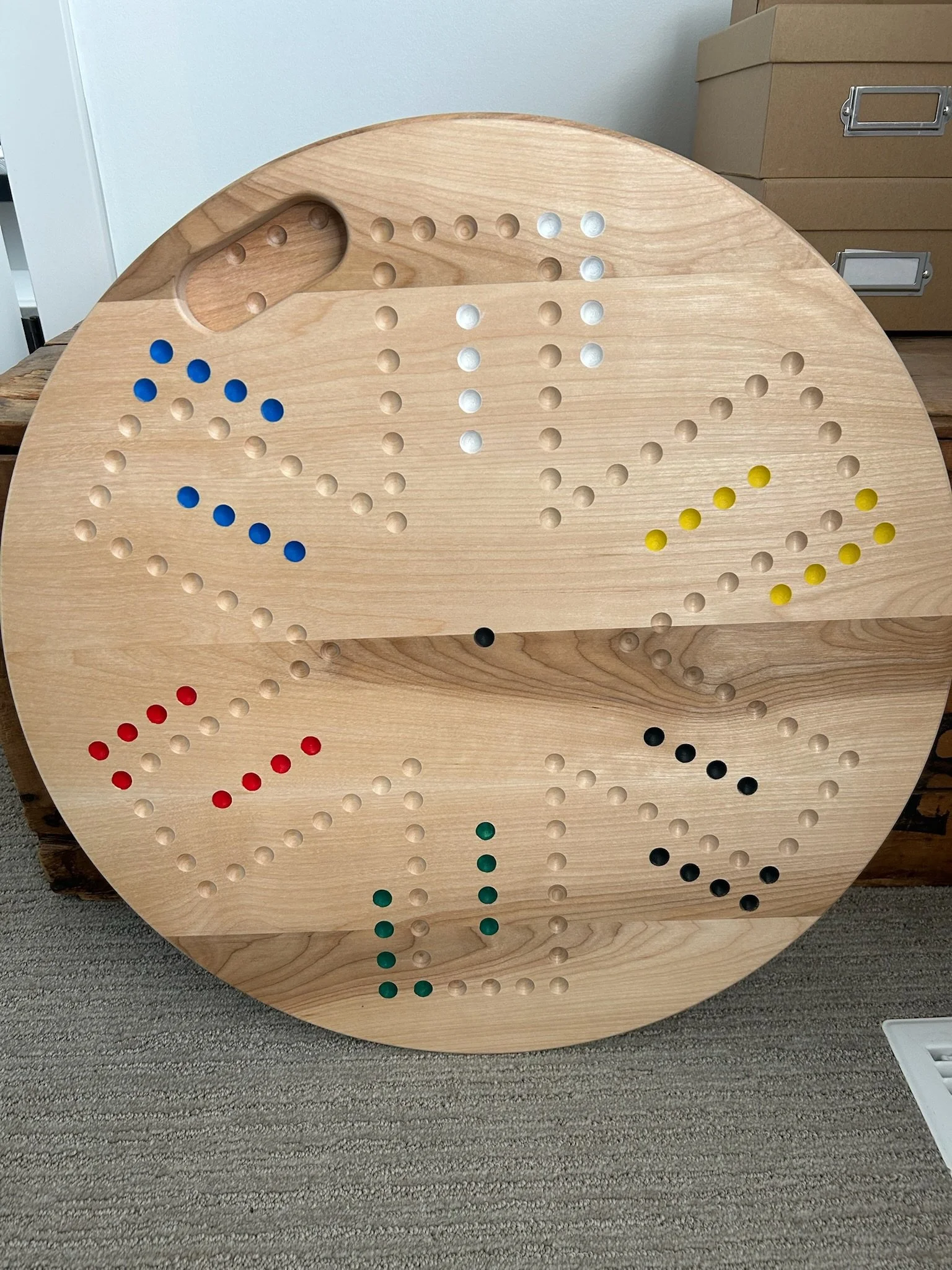 Round wooden board with a game of Connect Four, featuring red, blue, yellow, and green discs arranged in a pattern.