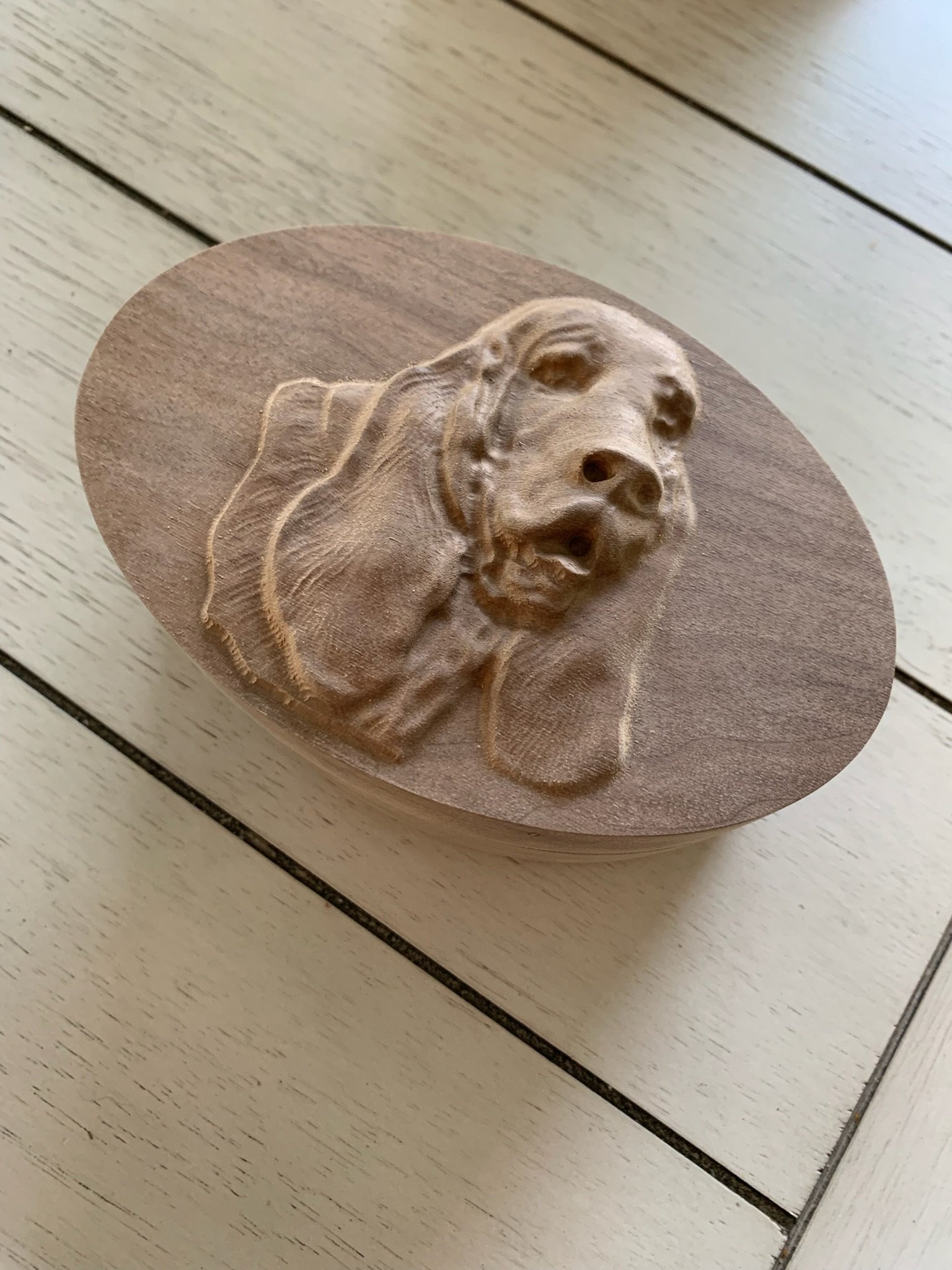 Wooden oval-shaped plaque with a carved Labrador Retriever dog's head in profile, placed on a light wooden floor.