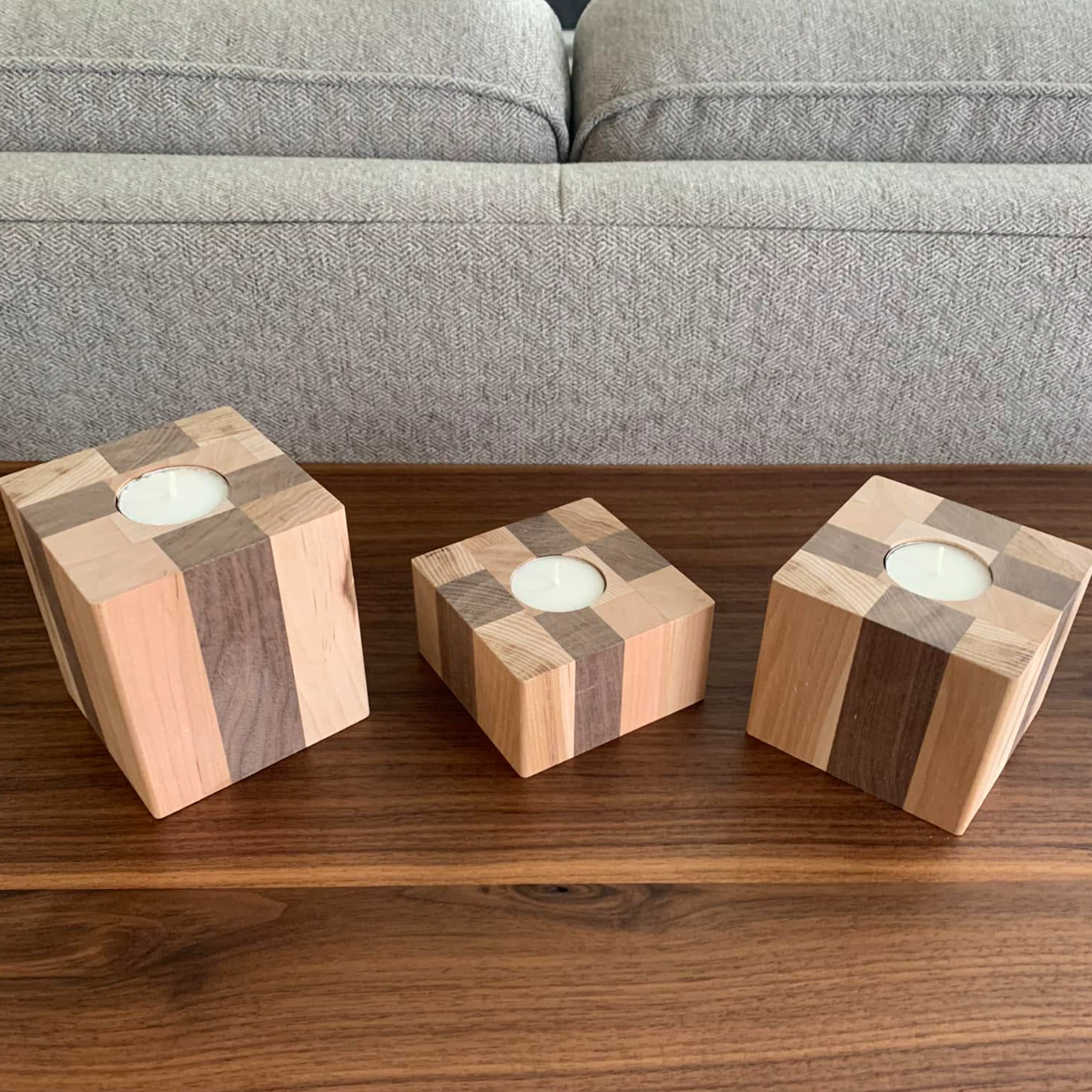Three wooden candle holders of different sizes with geometric patterns on a wooden table, with a gray fabric sofa in the background.