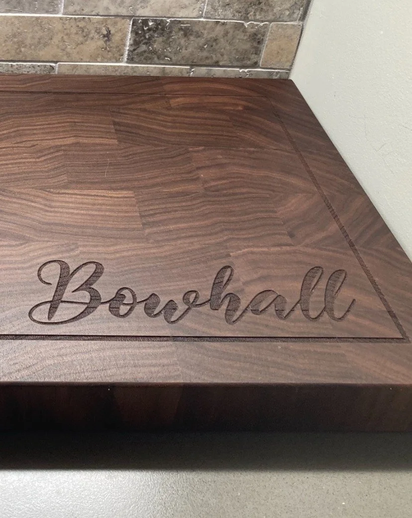 Wooden box with the word "Bougain" engraved on the lid, placed on a gray surface with brick wall background.
