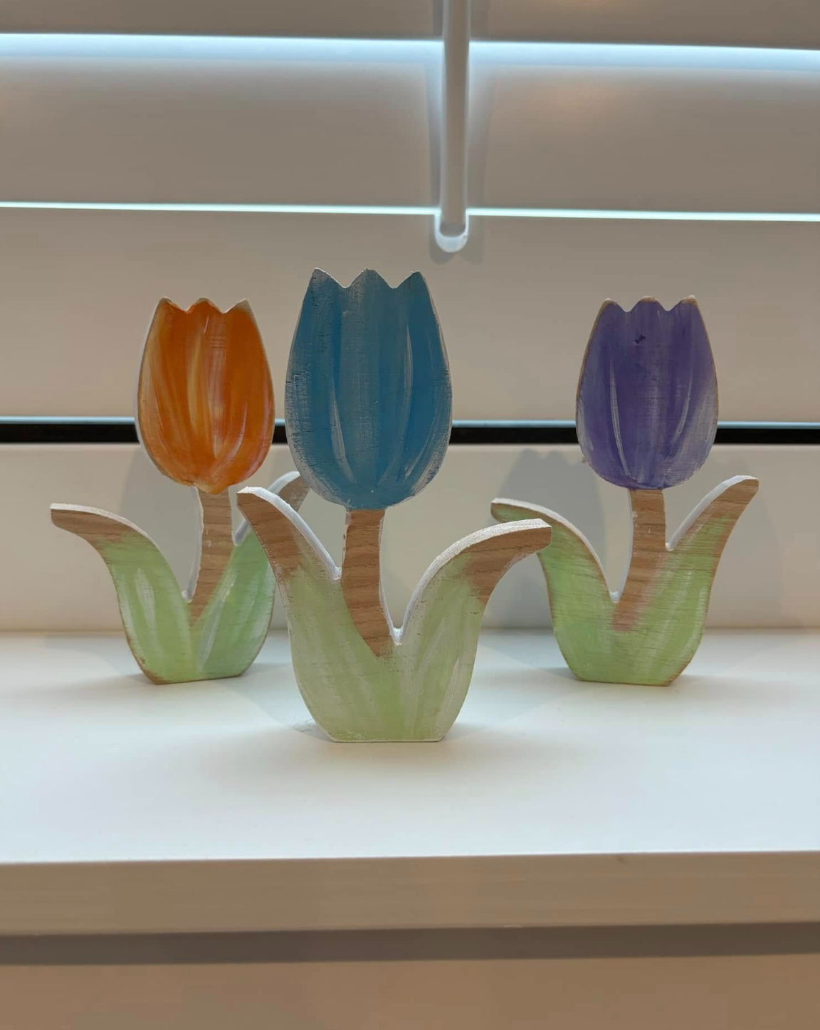 Decorative wooden tulip flowers painted in orange, blue, and purple, with green leaves, arranged in a row on a white surface.