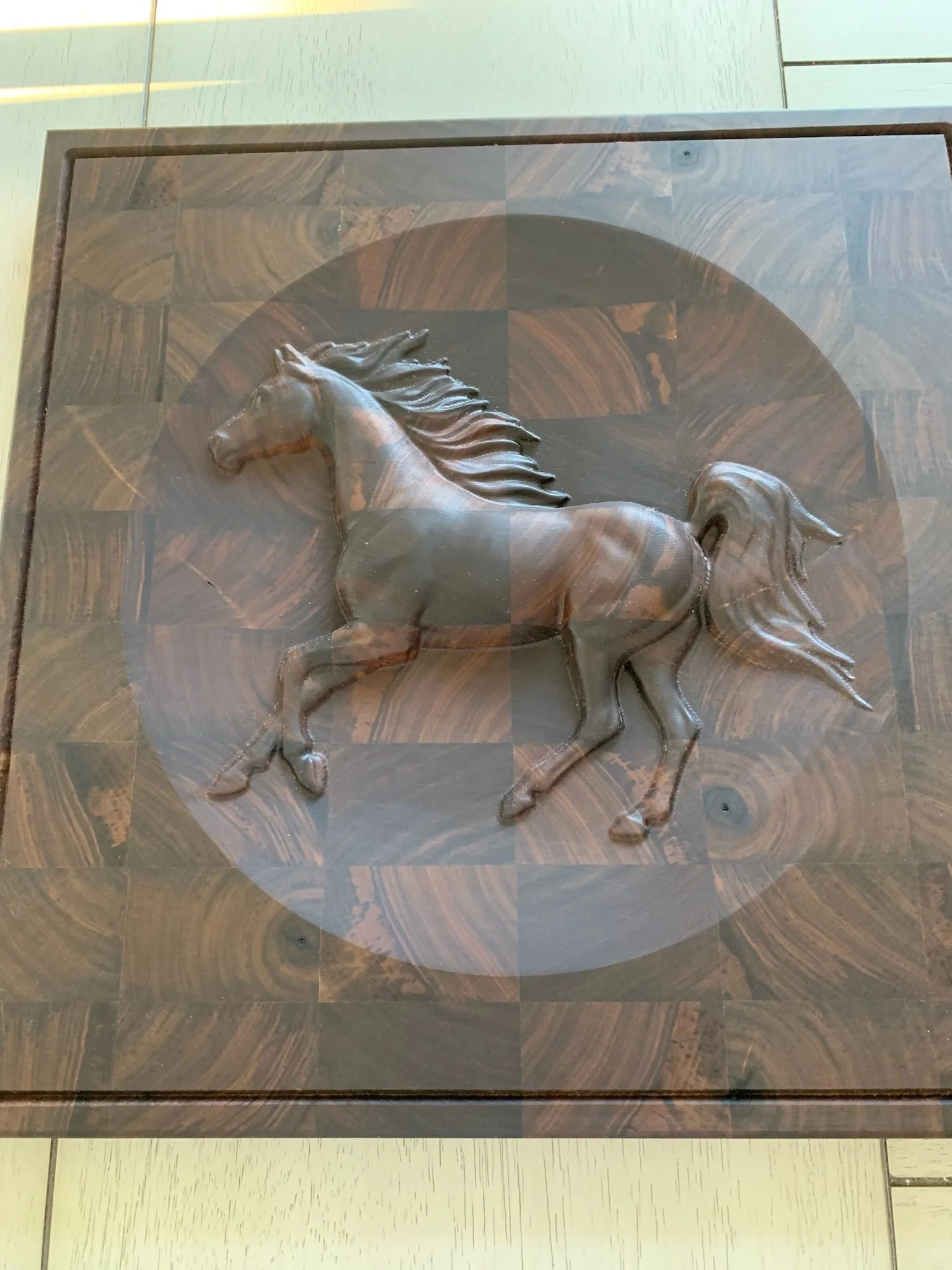 Wooden box with a 3D horse figure carved on top, placed on a tiled floor.