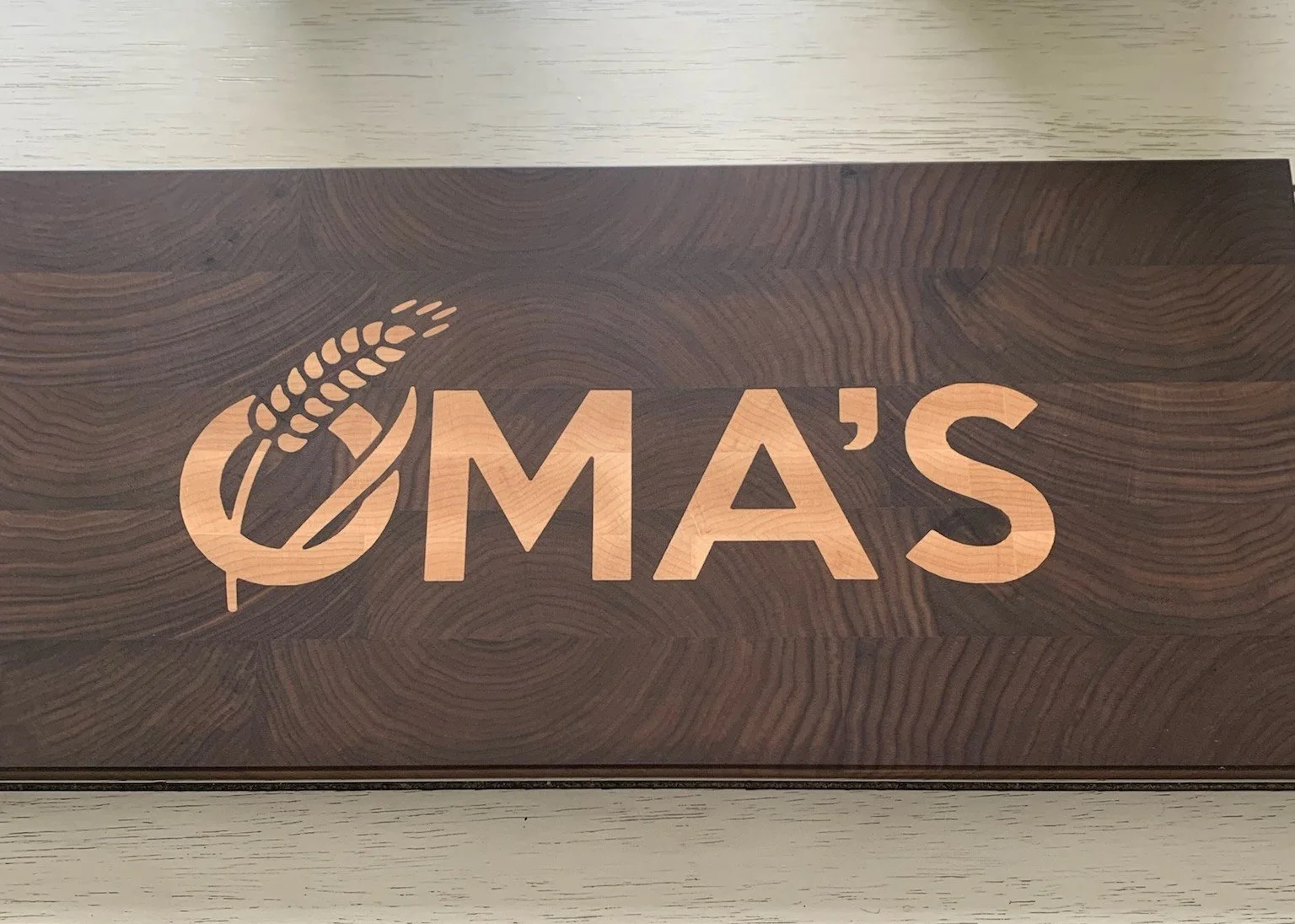 Wooden sign with the logo and text 'OMA'S' and a stylized wheat stalk.