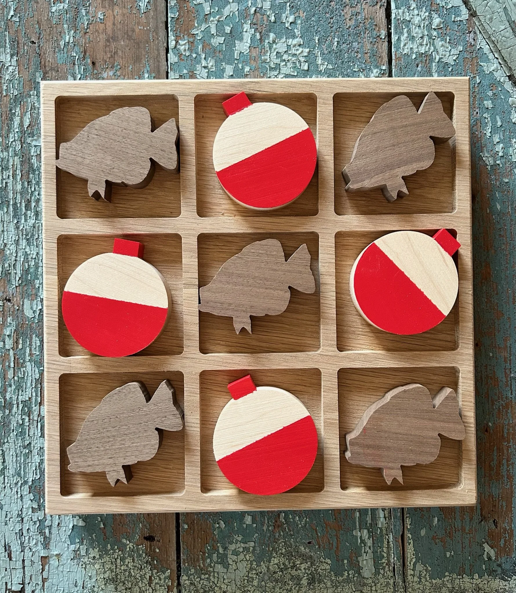 A wooden tic-tac-toe board with three matches, shaped like leaves, and three painted wooden pieces, shaped like Christmas ornaments, with red and white stripes, placed in a 3x3 grid on a rustic, lightly weathered paint-peeling wooden surface.