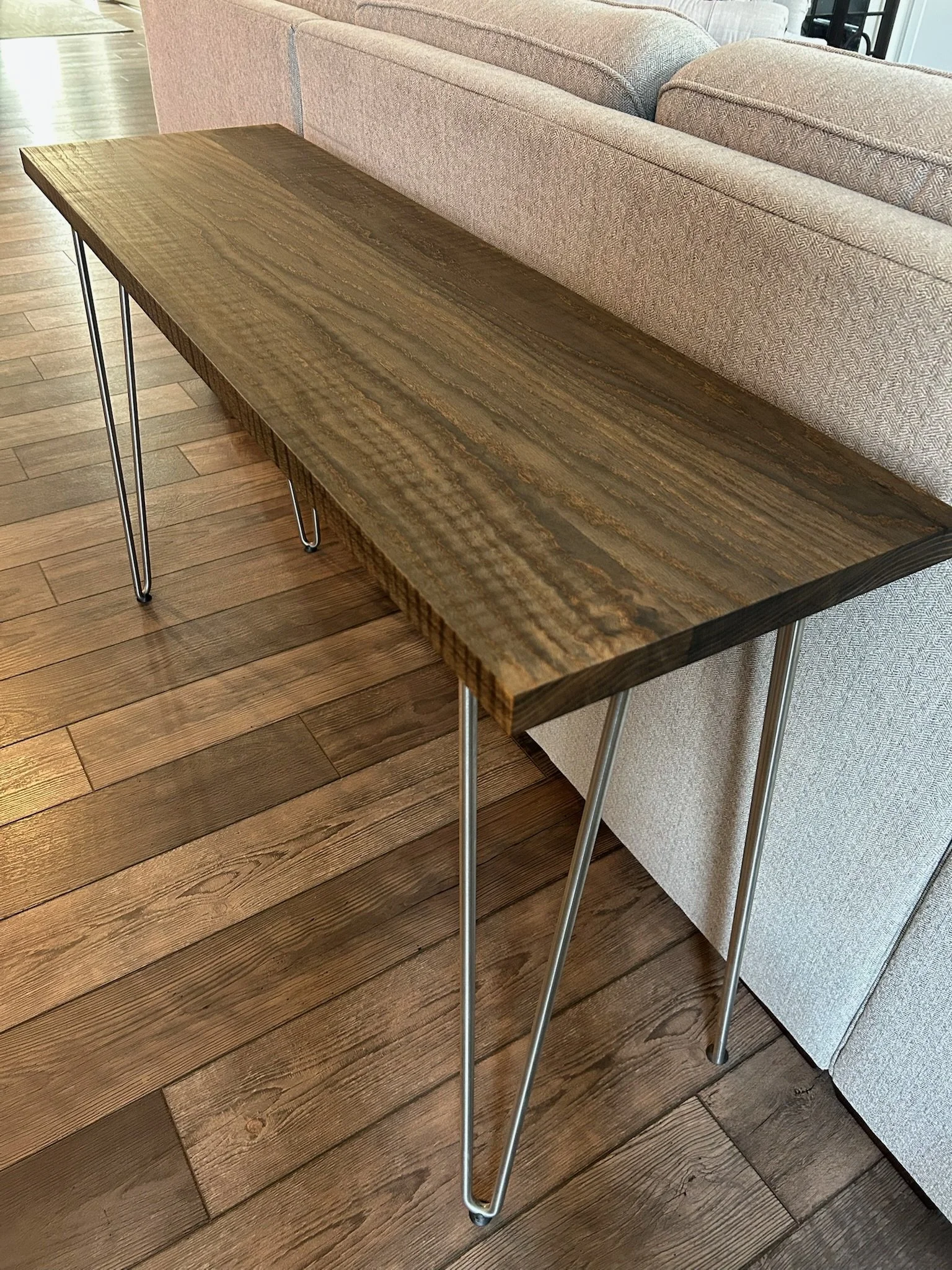 A wooden table with metal hairpin legs placed in a living room with a wooden floor and a sofa.