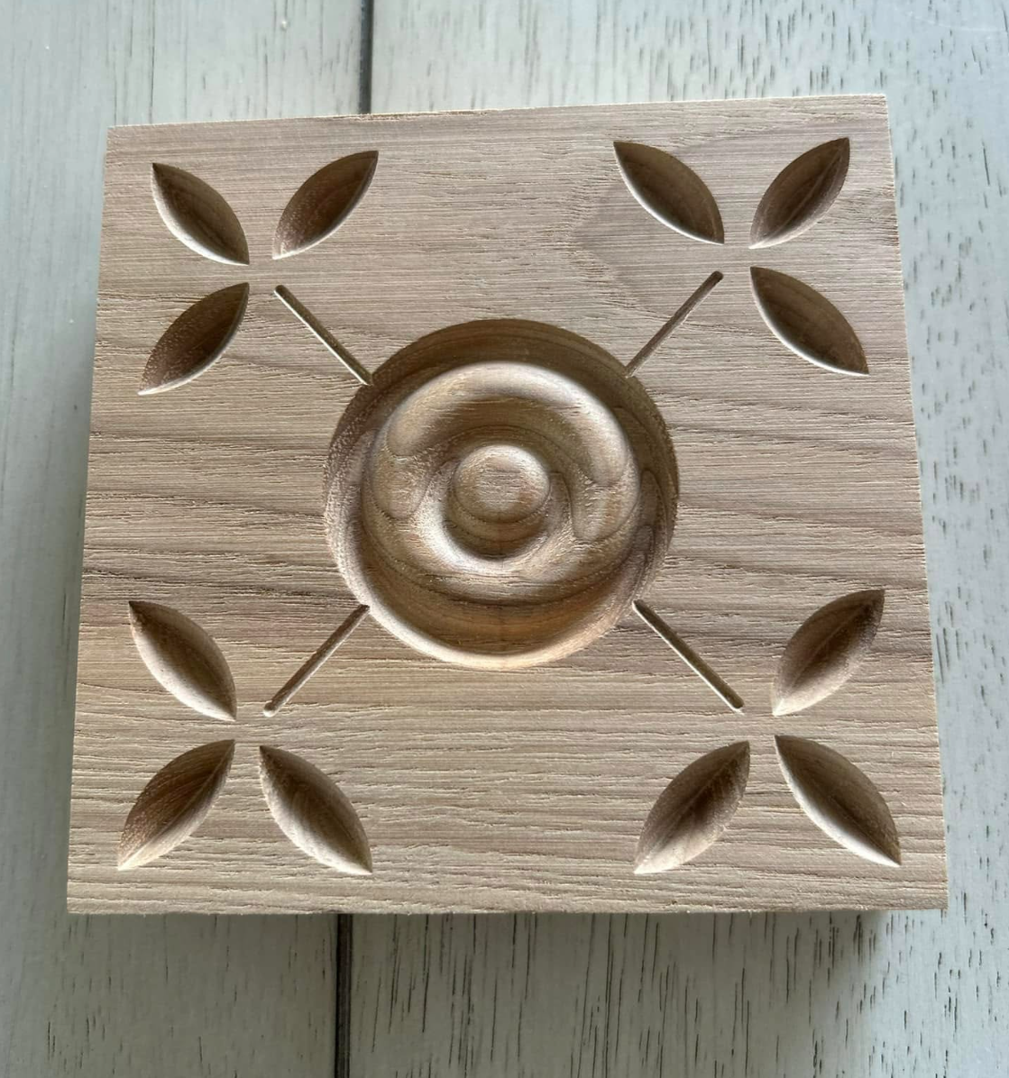 A wooden board with carved slots and a spiral-shaped indentation in the center, designed to hold small objects, with leaf-shaped cutouts around the central spiral.