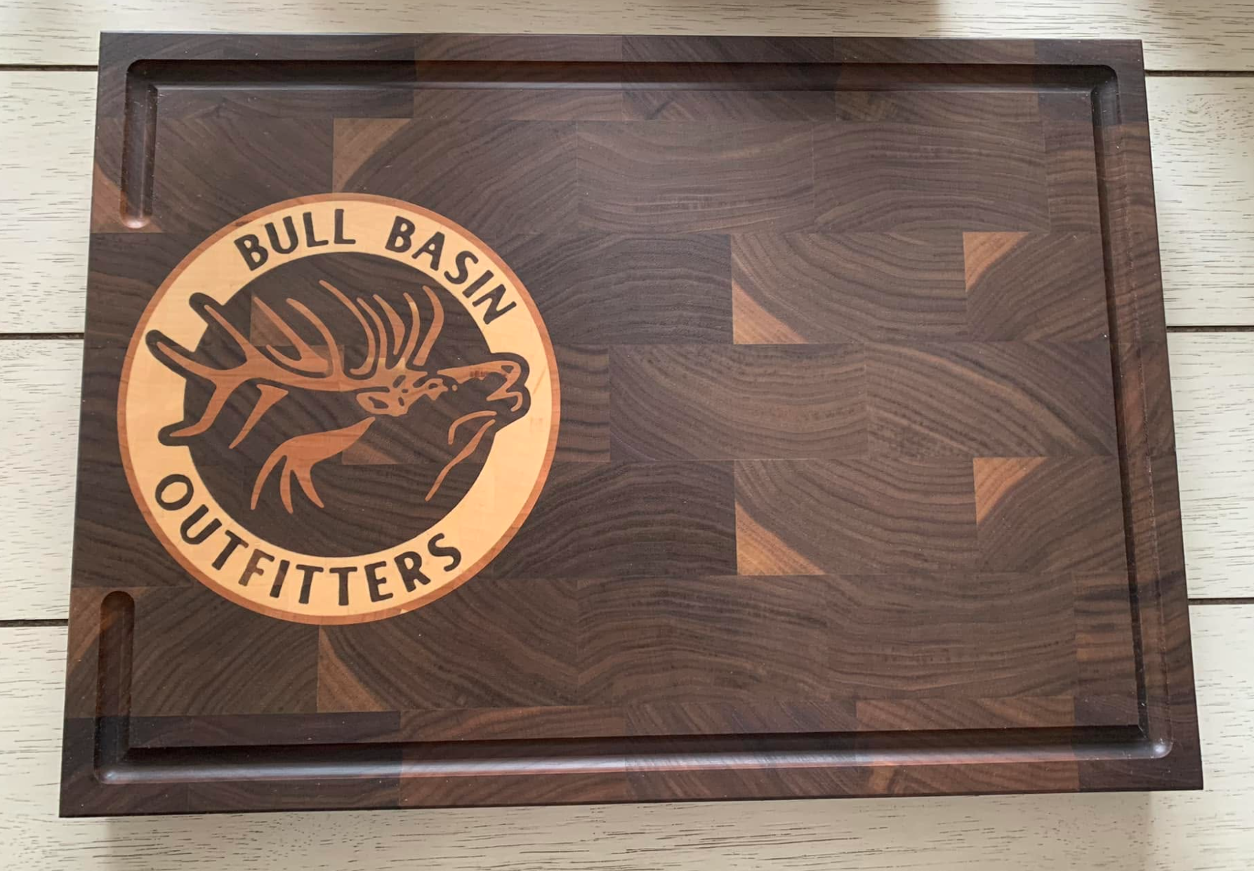 A wooden tray with a logo for Bull Bull Basih Outfitters, featuring a stylized elk head with antlers.