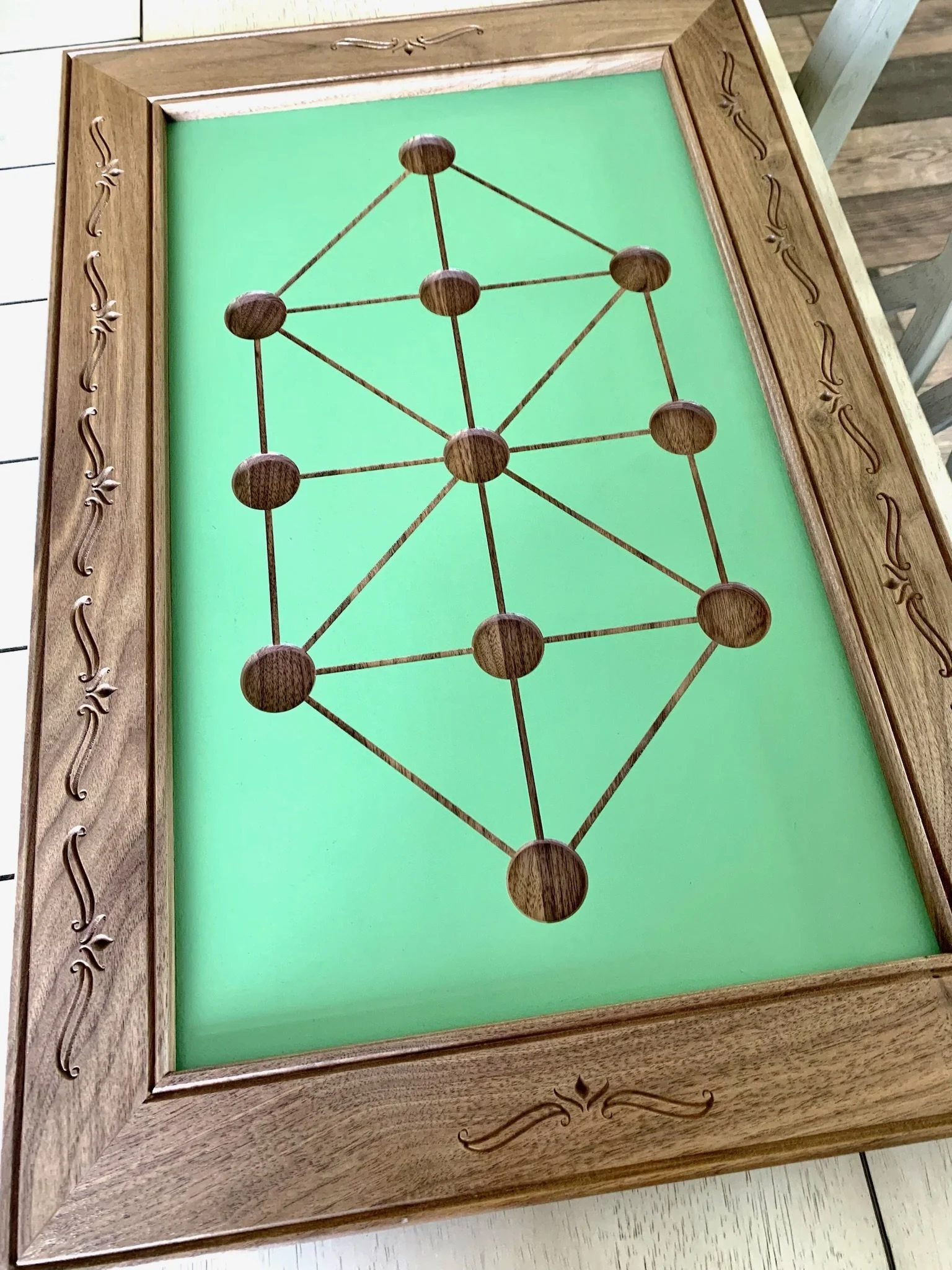 Wooden tabletop with a green background and a network of connected wooden dots, surrounded by a carved wooden border.
