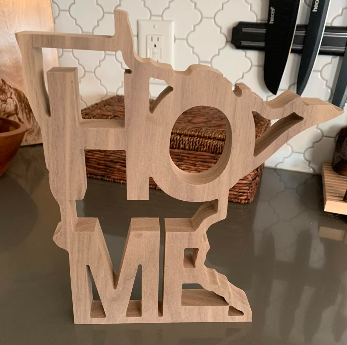 Wooden decorative piece spelling the word "HOME" with a heart-shaped cutout in the "O."