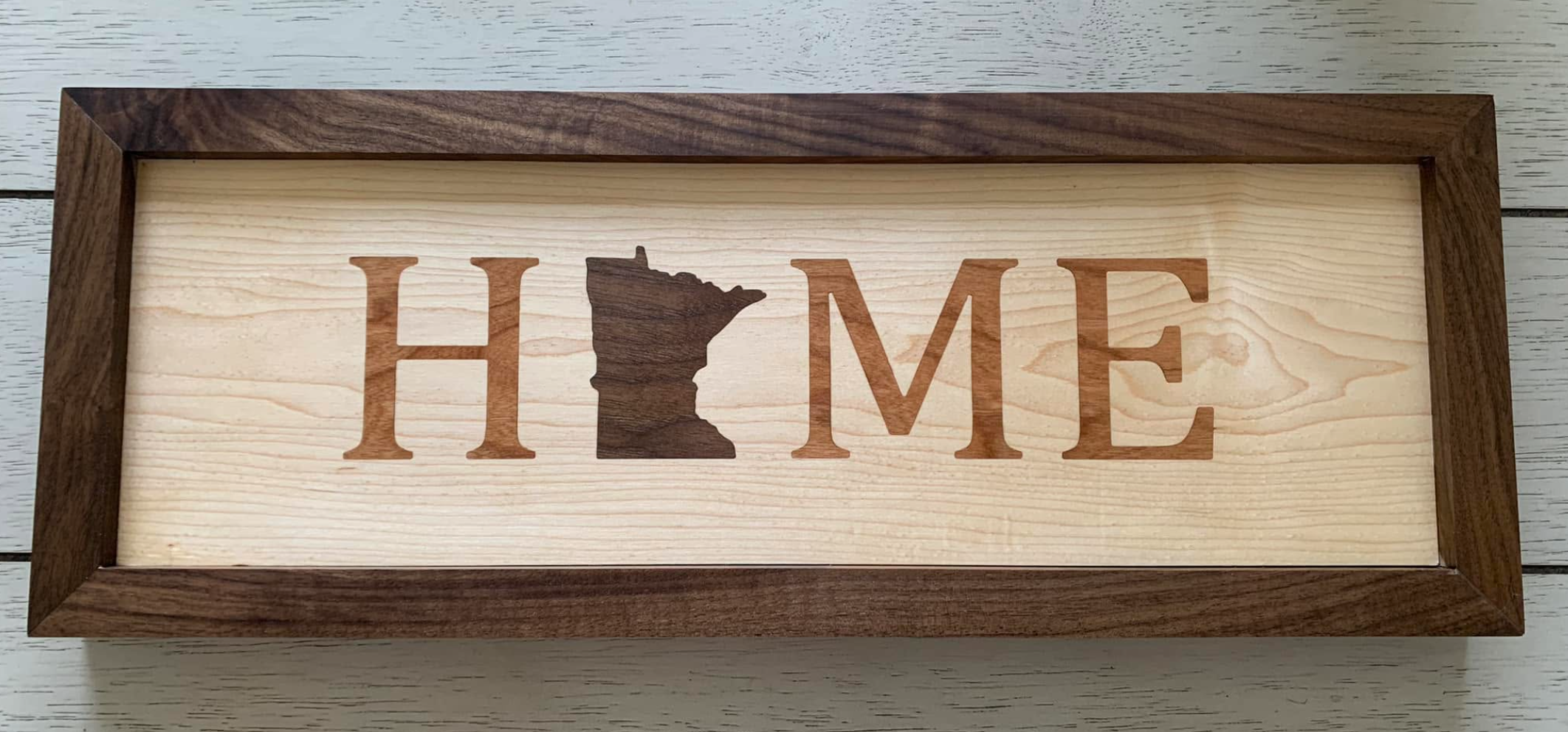 Wooden framed sign with the word 'HOME' spelled out, with the letter 'O' replaced by the state of Minnesota's outline.