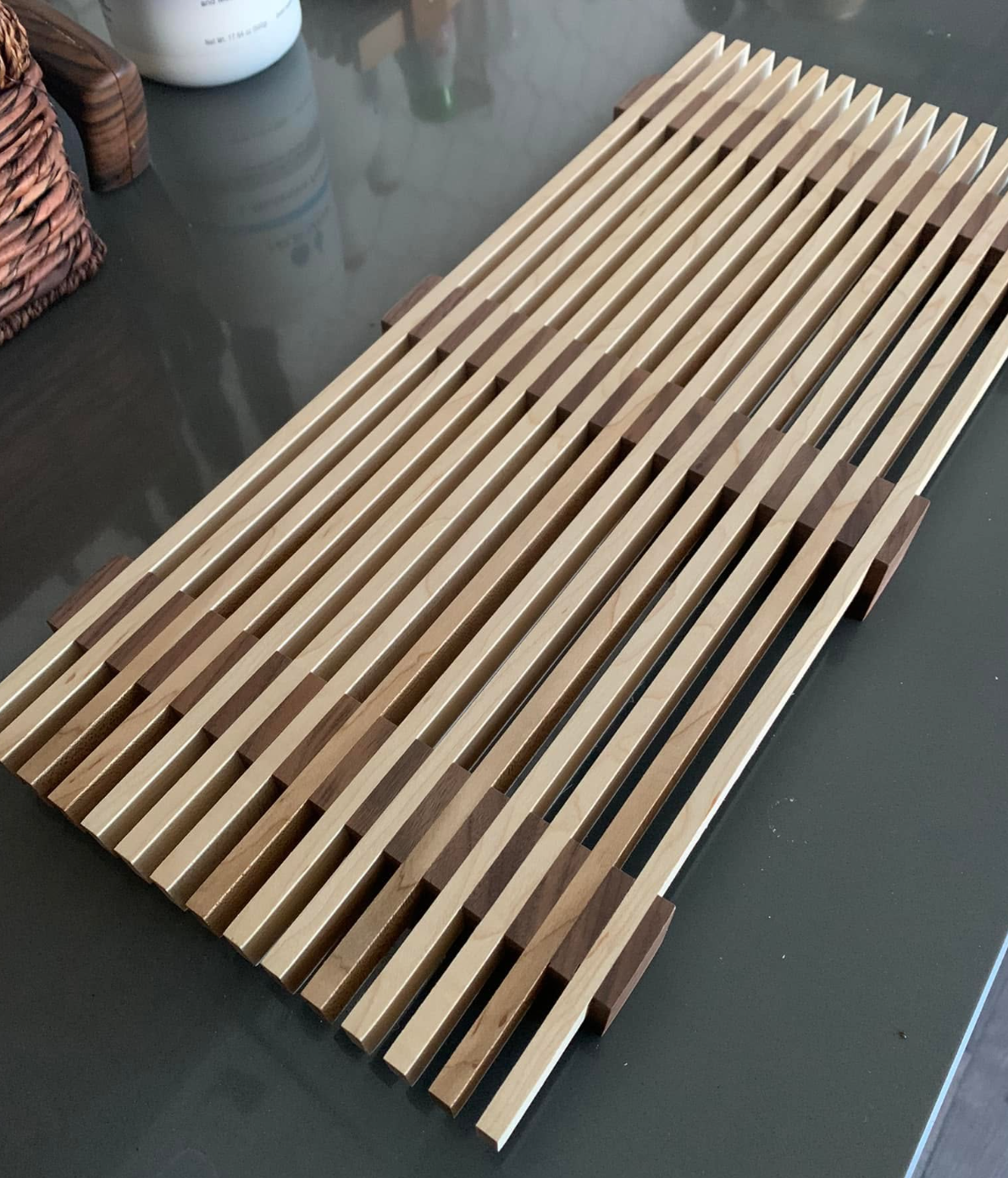 A wooden slatted bench with alternating light and dark wood. The slats are evenly spaced and rests on a black surface.