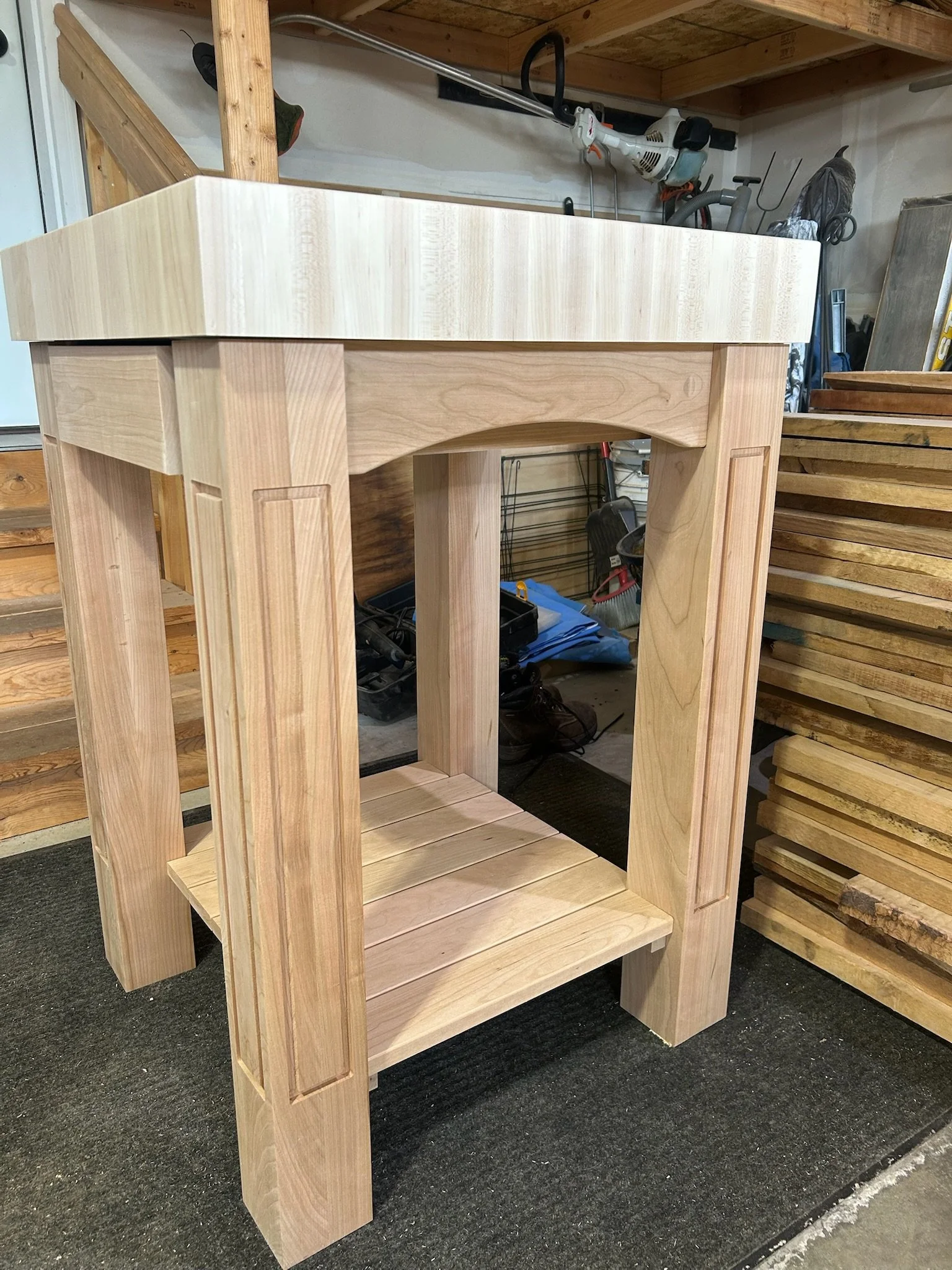 Unfinished wooden table frame in a woodworking shop, with various tools and wood planks in the background.