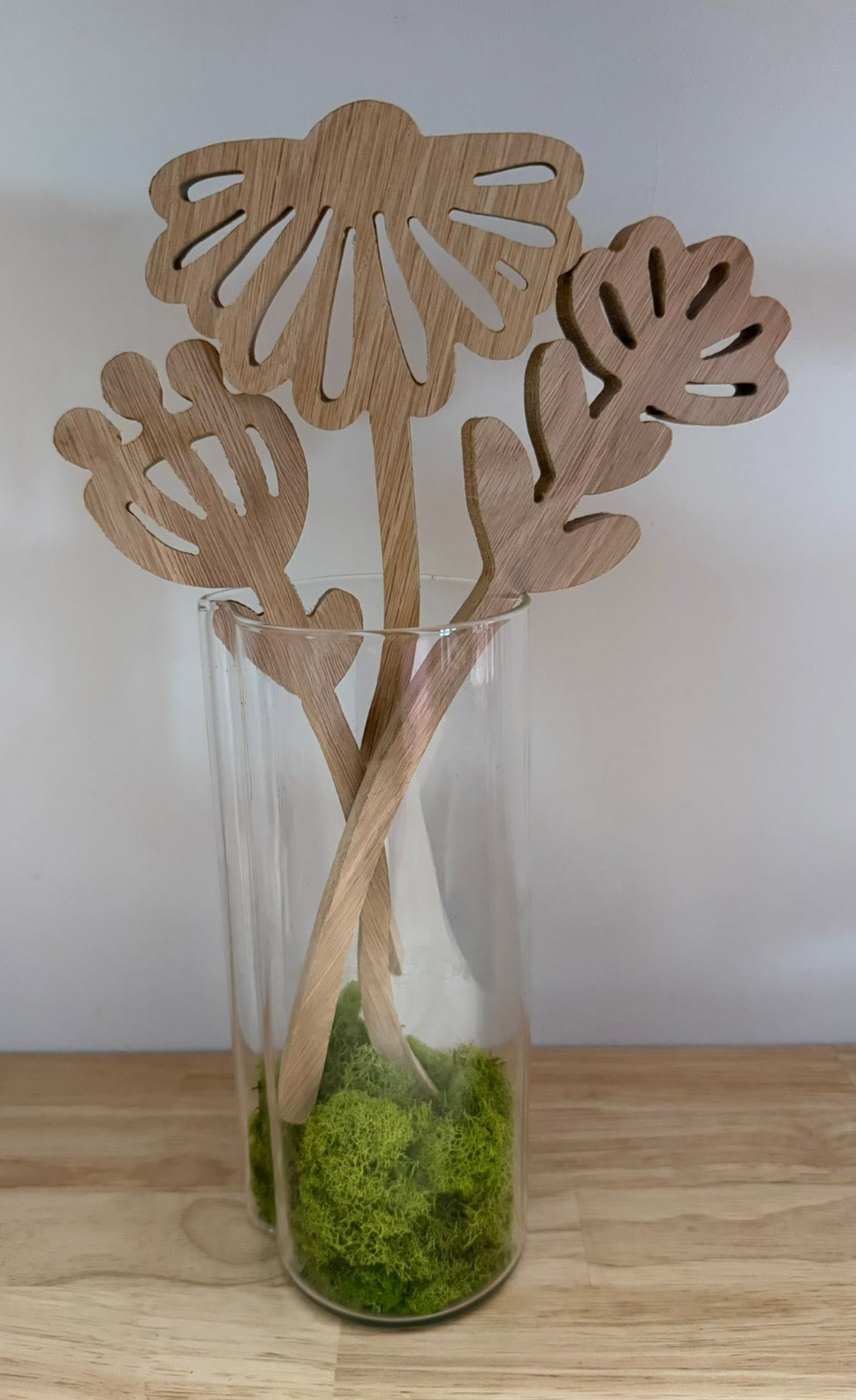 Wooden flower and leaf cutouts in a clear glass vase with green moss at the bottom.