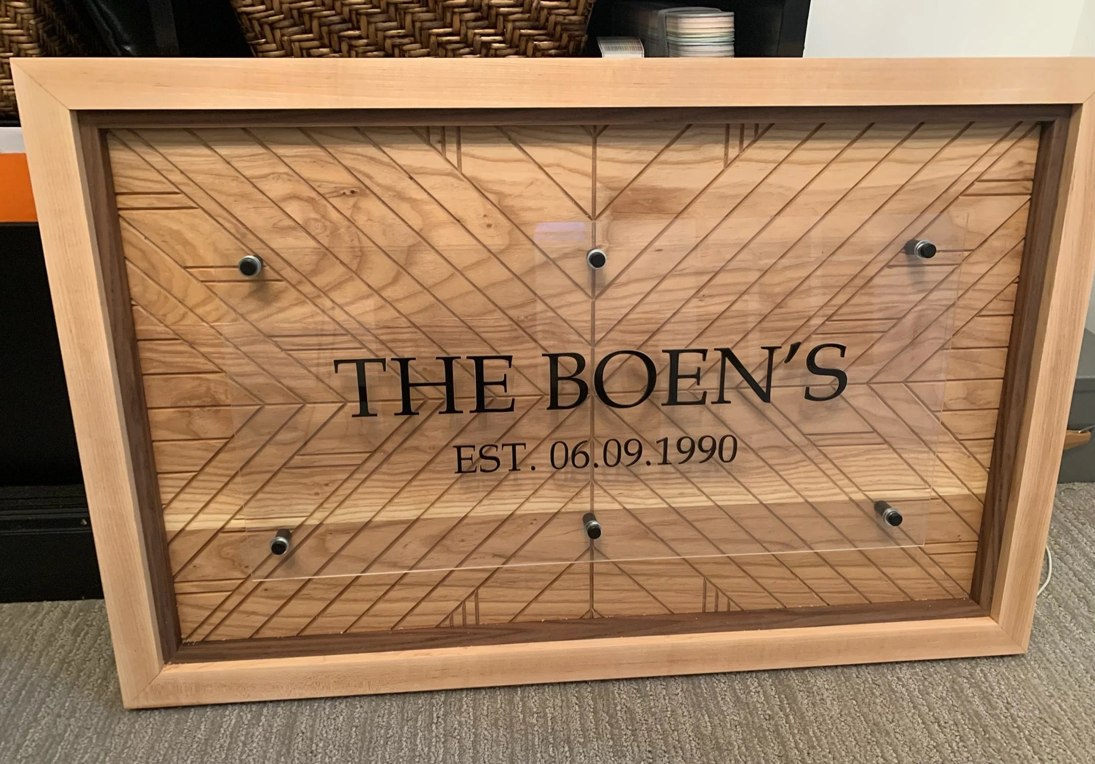 Wooden display stand with the text 'The Boen's' and 'Est. 06.09.1990' on the front. The background includes a stack of magazines or brochures.