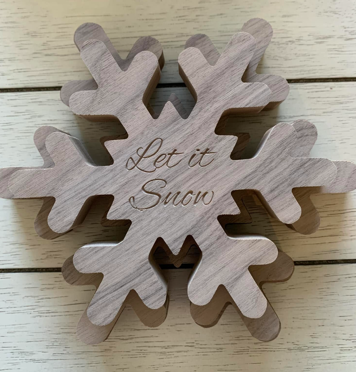 Wooden snowflake ornament with the engraved message "Let it Snow" on a white wooden surface.