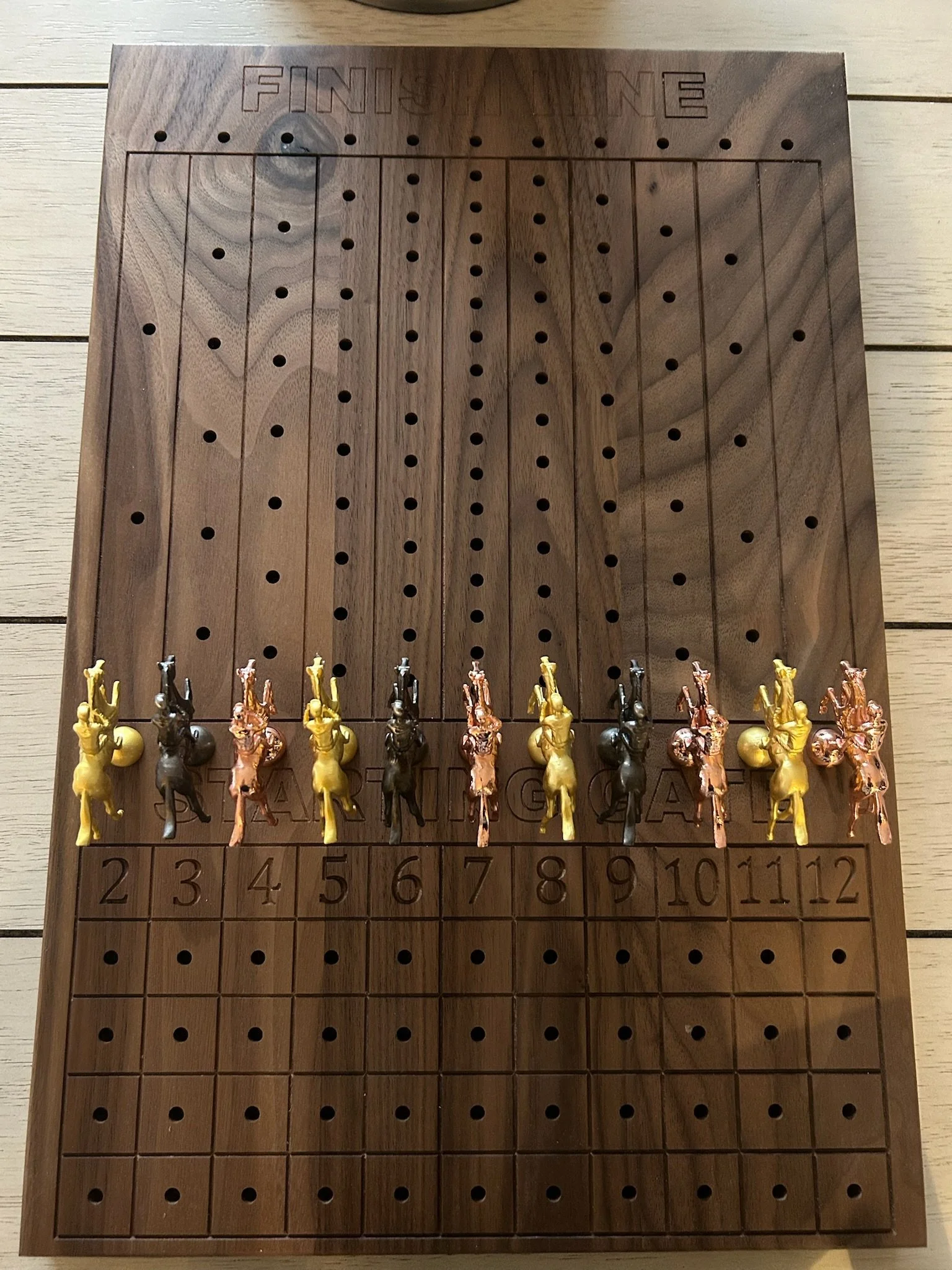 A wooden chessboard with the word 'FINISH' engraved at the top, but the checkered design is not visible. There are small plastic figures of chess pieces arranged in a line at the bottom edge of the board.