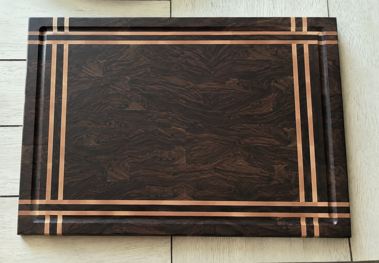 A rectangular wooden cutting board with a dark wood grain pattern and light wood inlay border, placed on a light wooden surface.