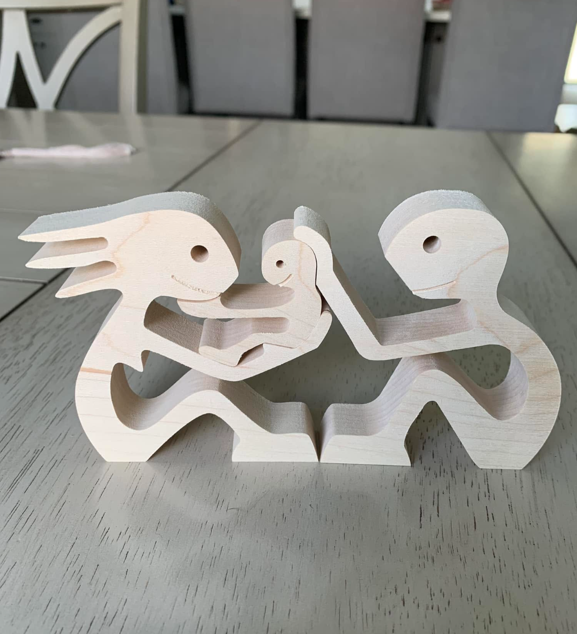 Wooden dinosaur figurines holding a small dinosaur in their hands, arranged in a face-to-face manner on a table.