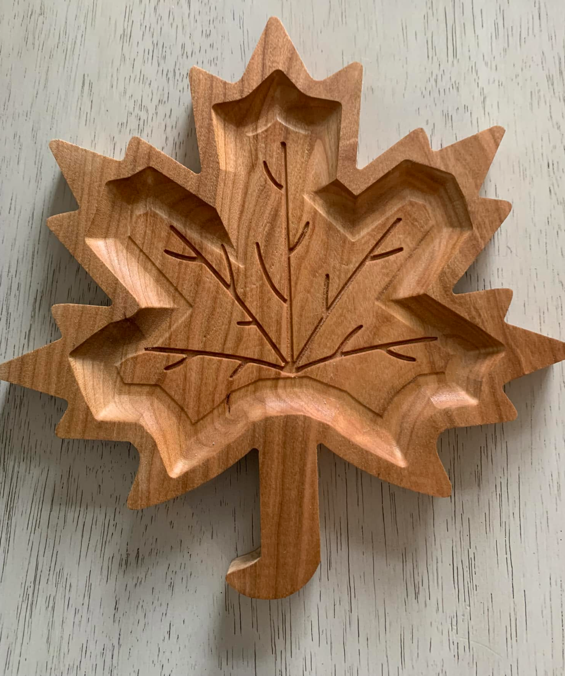 Wooden leaf-shaped container with engraved leaf veins, placed on a light-colored wooden surface.
