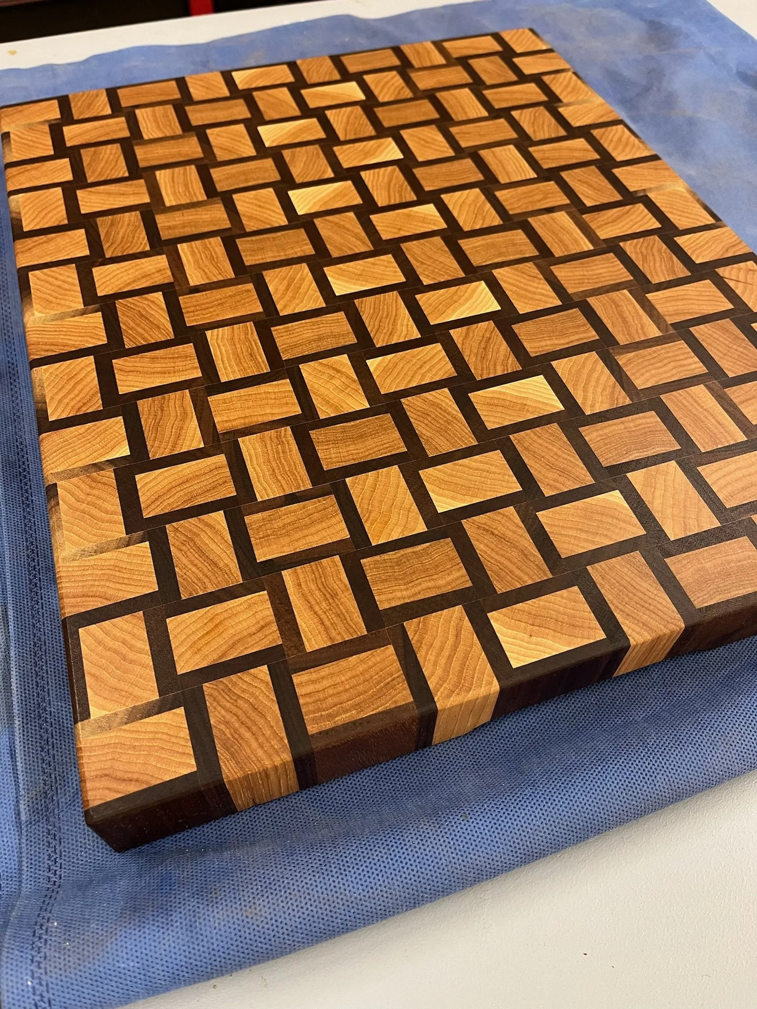 A wooden block with a checkered pattern of light and dark wood tiles, inset with dark wood strips.