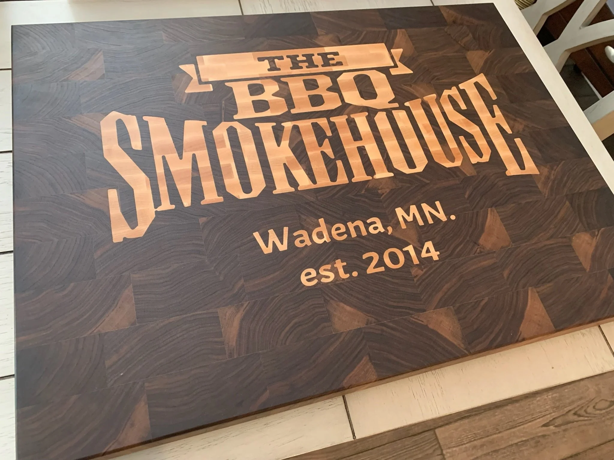 Wooden table with a printed design of the state of Minnesota and the words 'THE BIRON SHERIDAN Wadena, MN. est. 2014' in black and tan lettering.