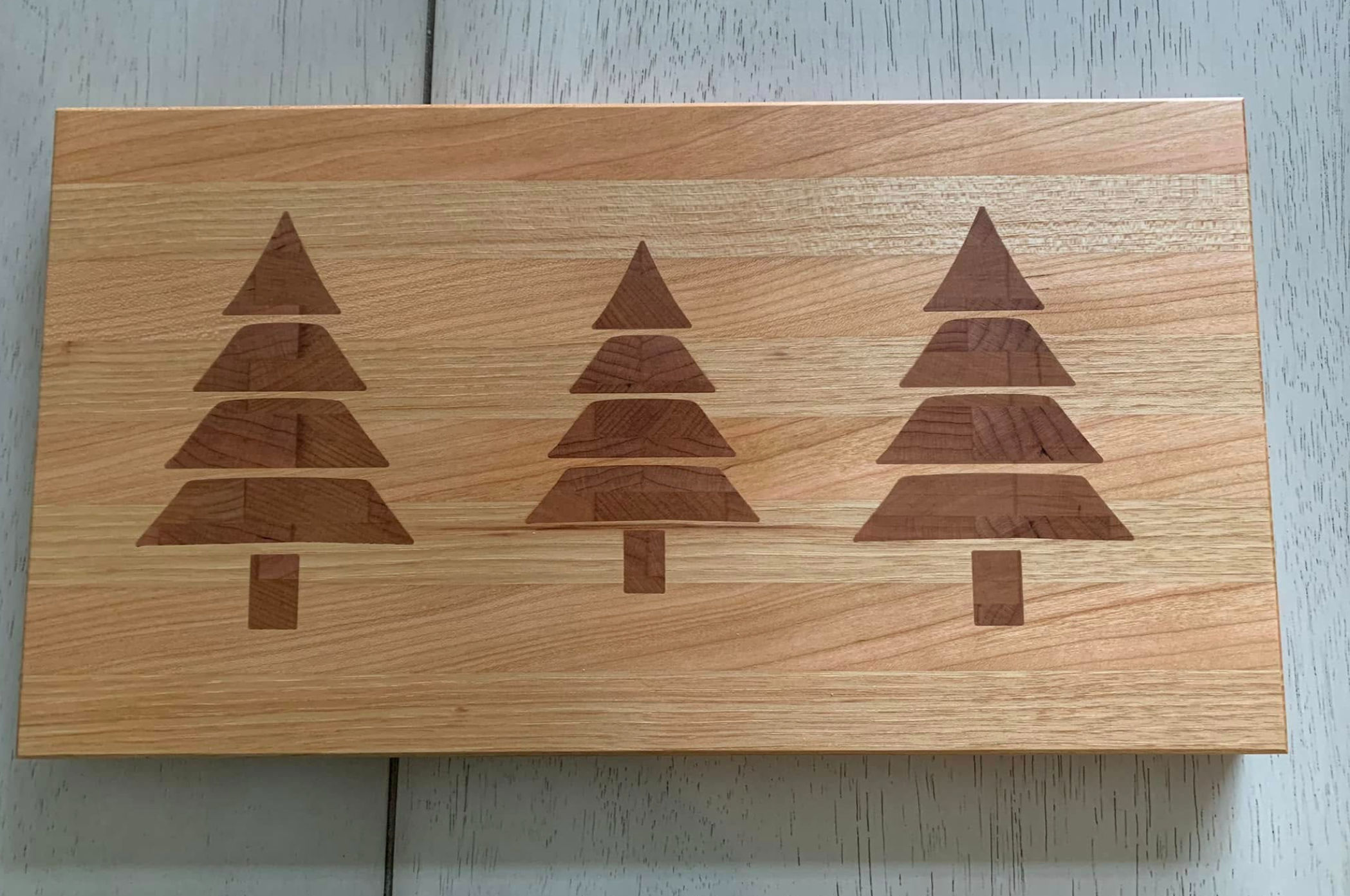 Wooden board with a pattern of three stylized trees, each made of different shades of wood, and small trunks beneath them.