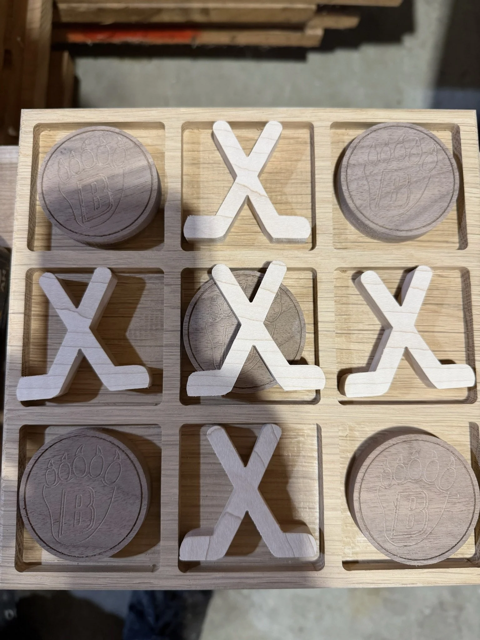 Wooden game pieces of coins with 'B' and numbers on them, and 'X' and check marks, arranged in a grid on a wooden board.