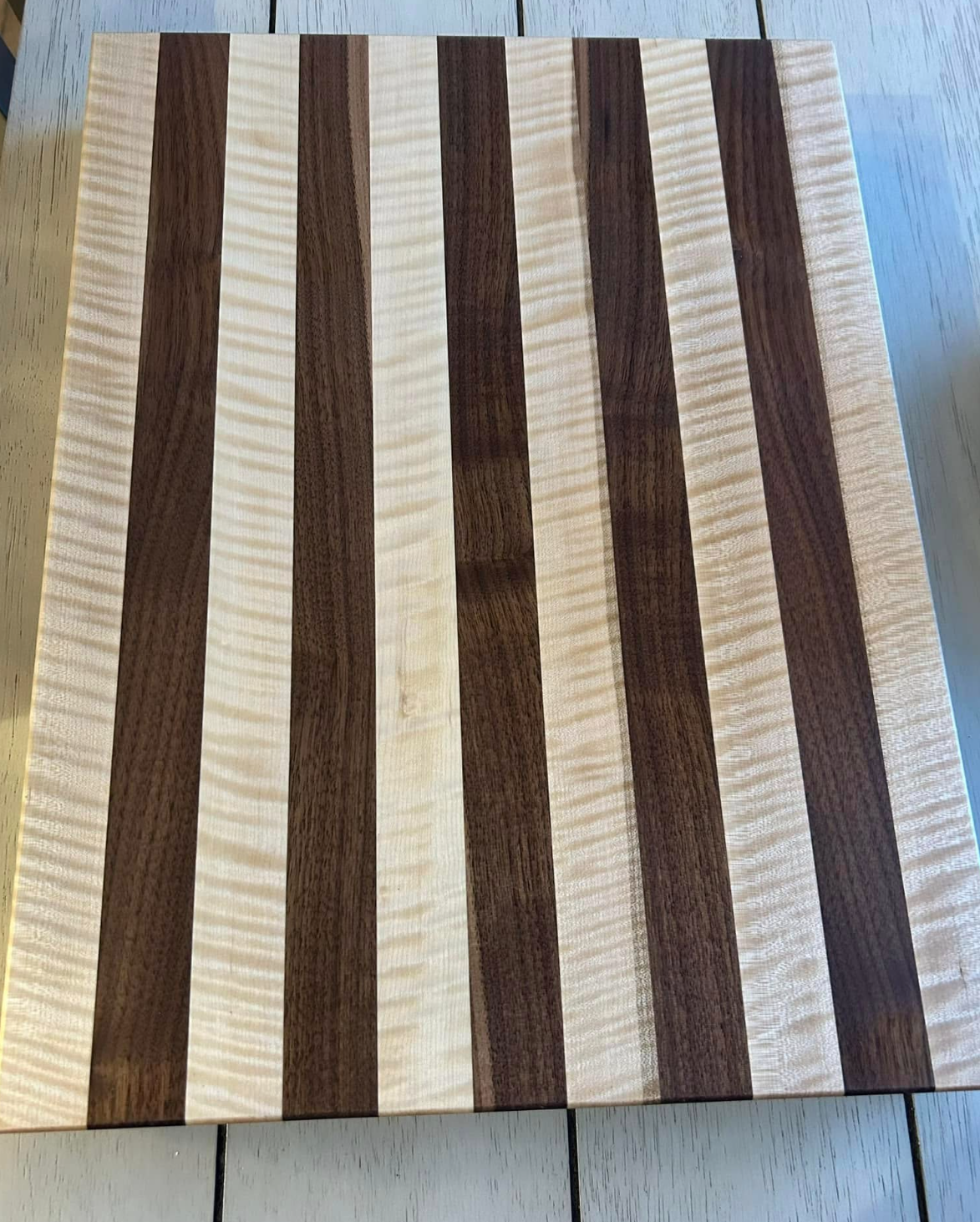 A wooden cutting board with alternating light and dark wood stripes placed on a tiled surface.