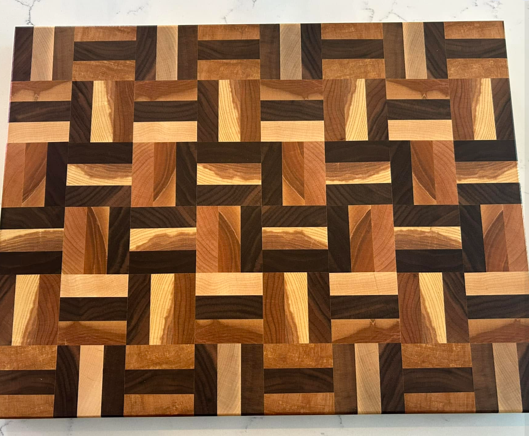 A wooden cutting board with an intricate geometric pattern made of alternating light and dark wood squares.