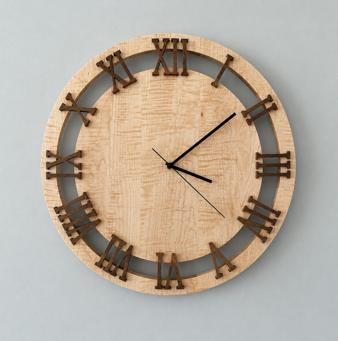Round wooden wall clock with Roman numerals, black hour and minute hands, and a gray background, hanging on a light gray wall.