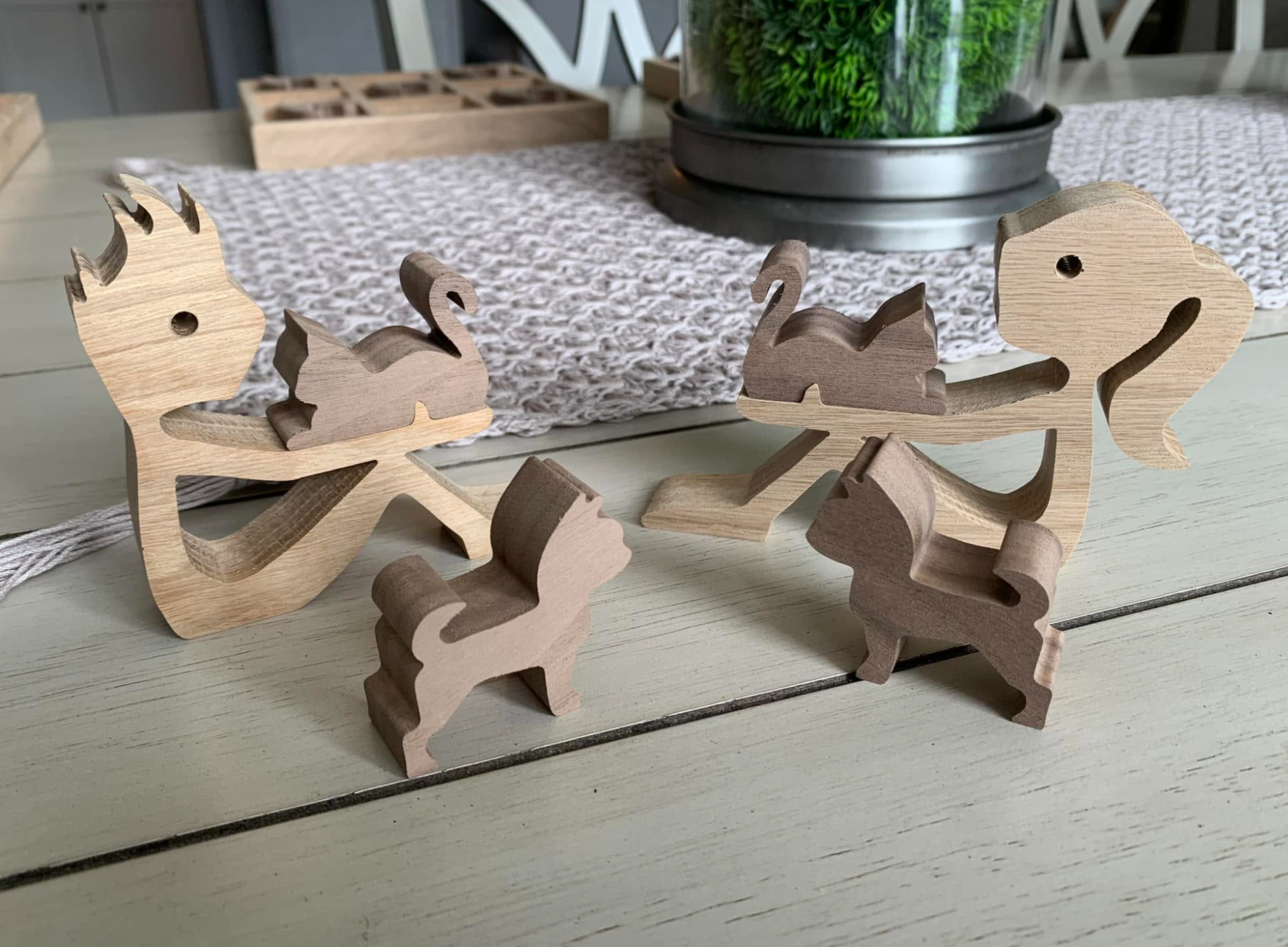 Wooden animal-shaped puzzle pieces arranged on a white table, with a woven table runner and potted green plant in the background.