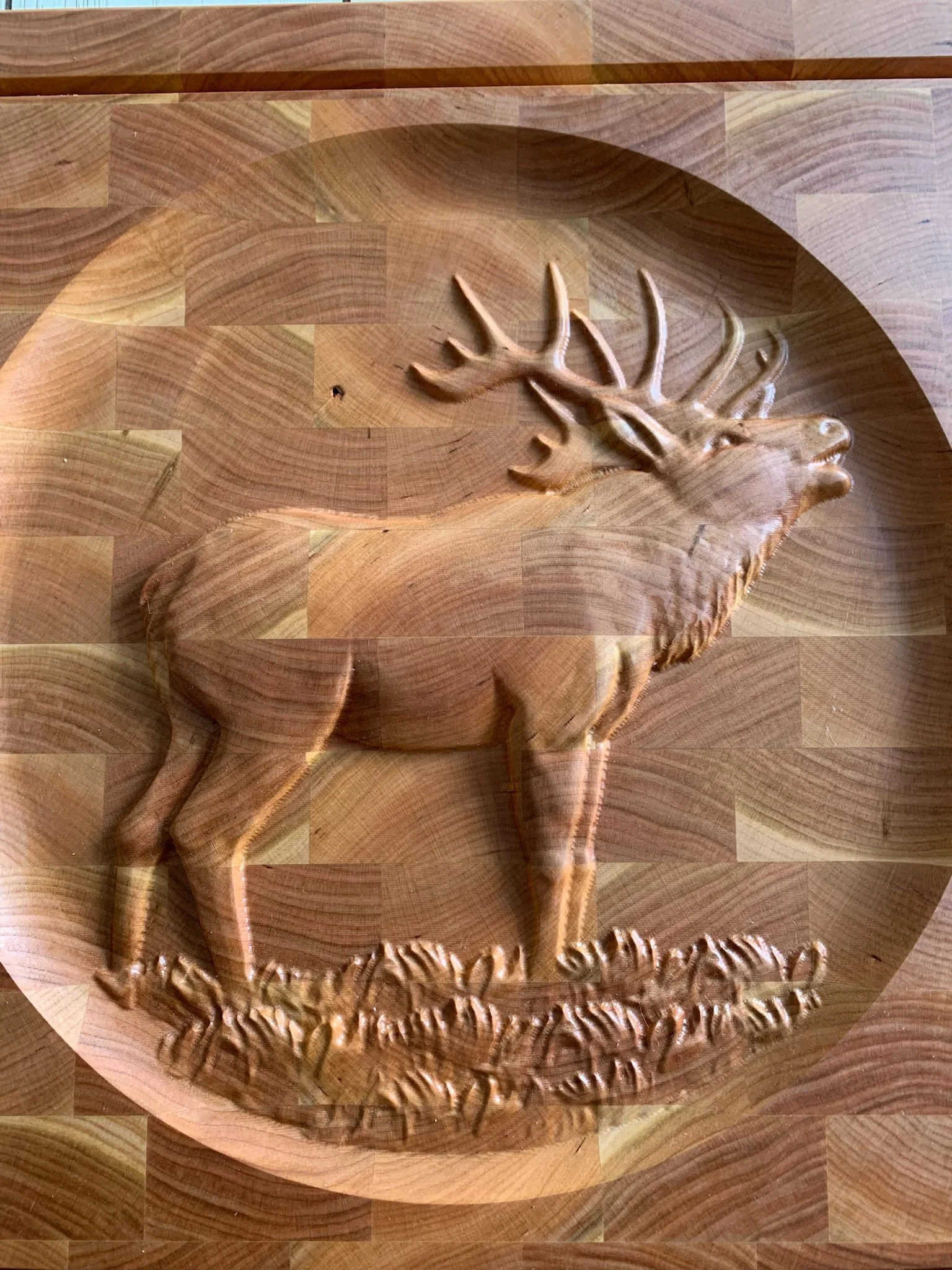 A carved wooden piece featuring a deer with antlers inside an oval shape, on a wooden surface.