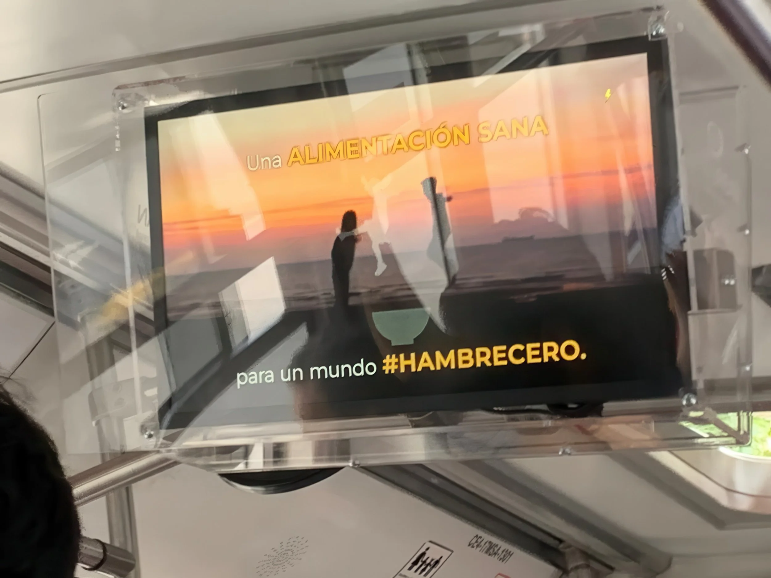 A digital screen displaying a sunset with orange, pink, and purple hues, and silhouettes of a person and trees, with text in Spanish that reads 'Una ALIMENTACIÓN SANA' over the sunset and additional text at the bottom.