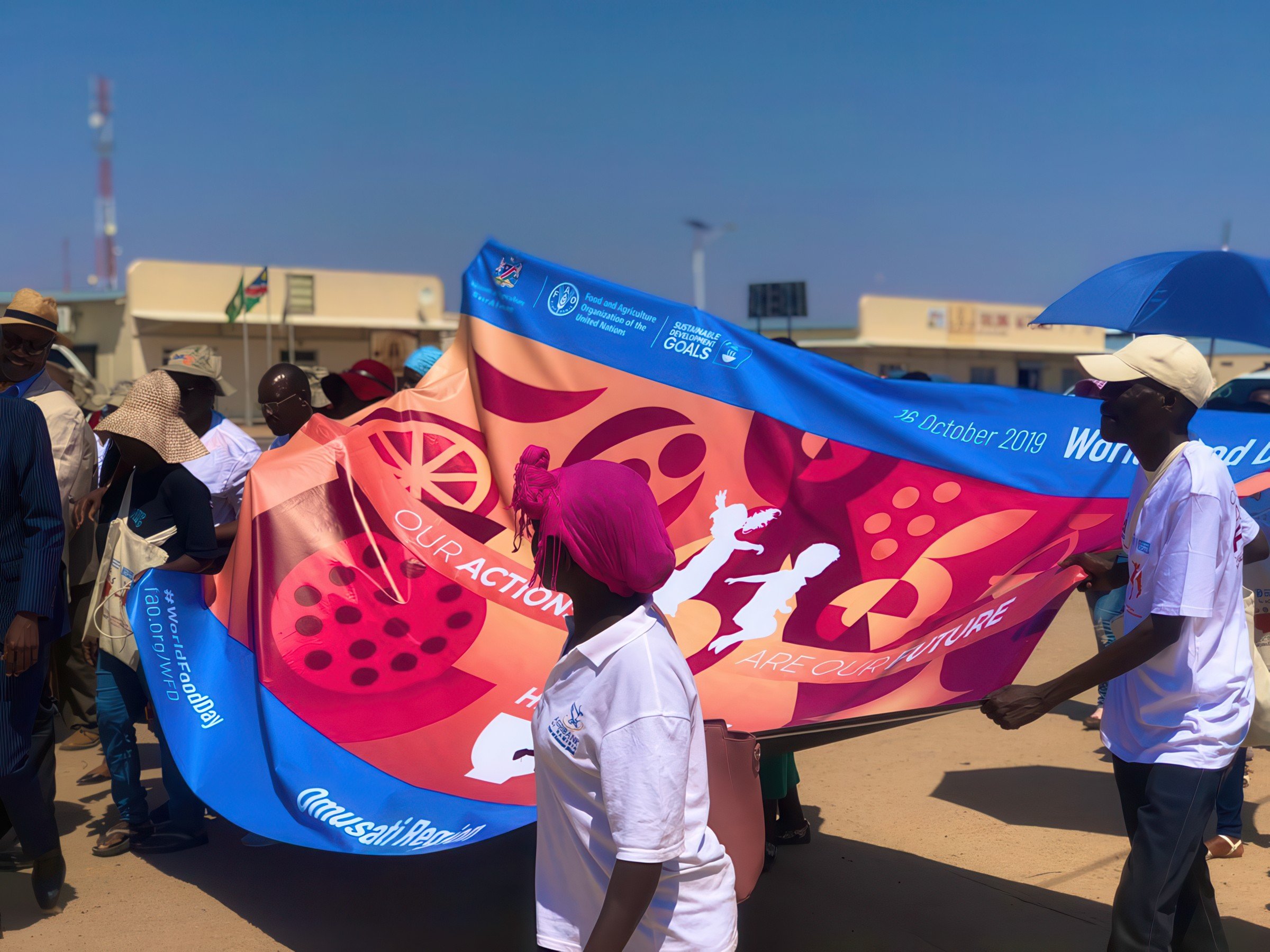 Group of people participating in an outdoor event holding a large colorful banner with the United Nations Food and Agriculture Organization (FAO) logo and the text 'OUR ACTION FOR FUTURE'.