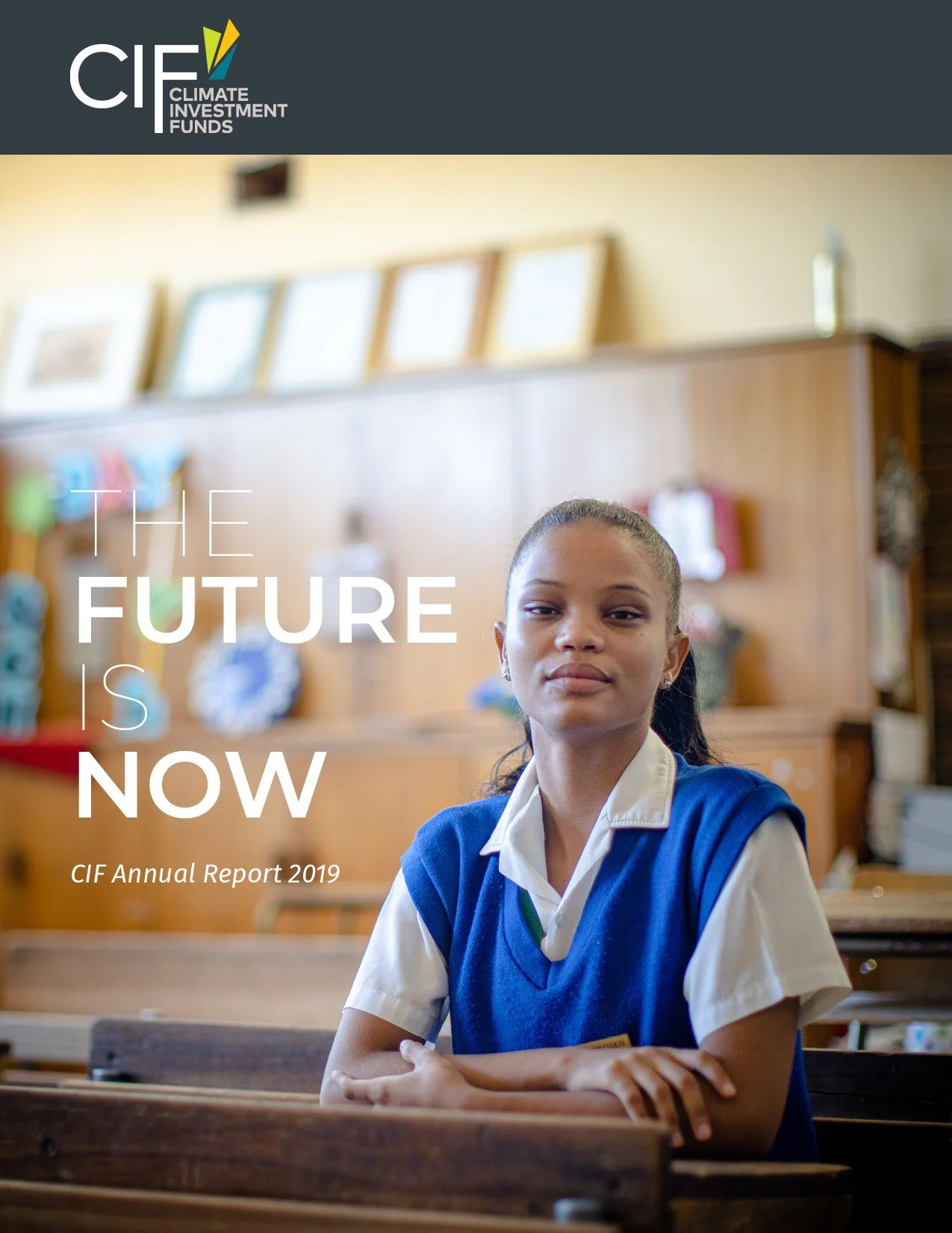 Cover of the CIF Annual Report 2019 featuring a young girl in a school uniform sitting at a desk in a classroom with a wooden backboard and some framed items on the wall behind her.
