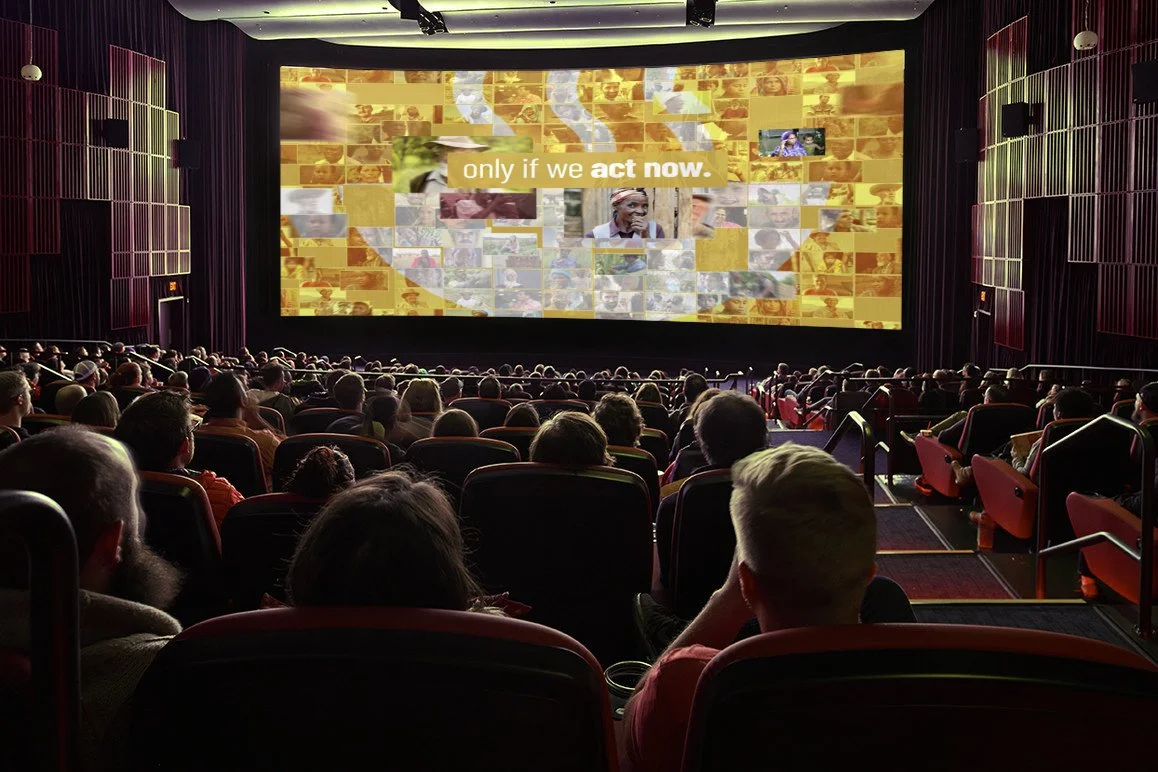 Audience watching a presentation or film in a movie theater with a large screen displaying a collage of images and text that reads 'only if we act now.'