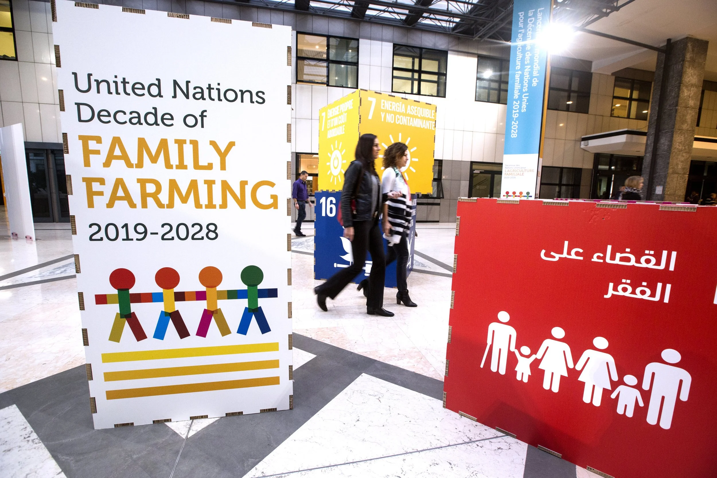 International exhibition hall with signs celebrating United Nations Decade of Family Farming from 2019 to 2028, featuring colorful graphics of people holding hands, and informational posters in multiple languages.