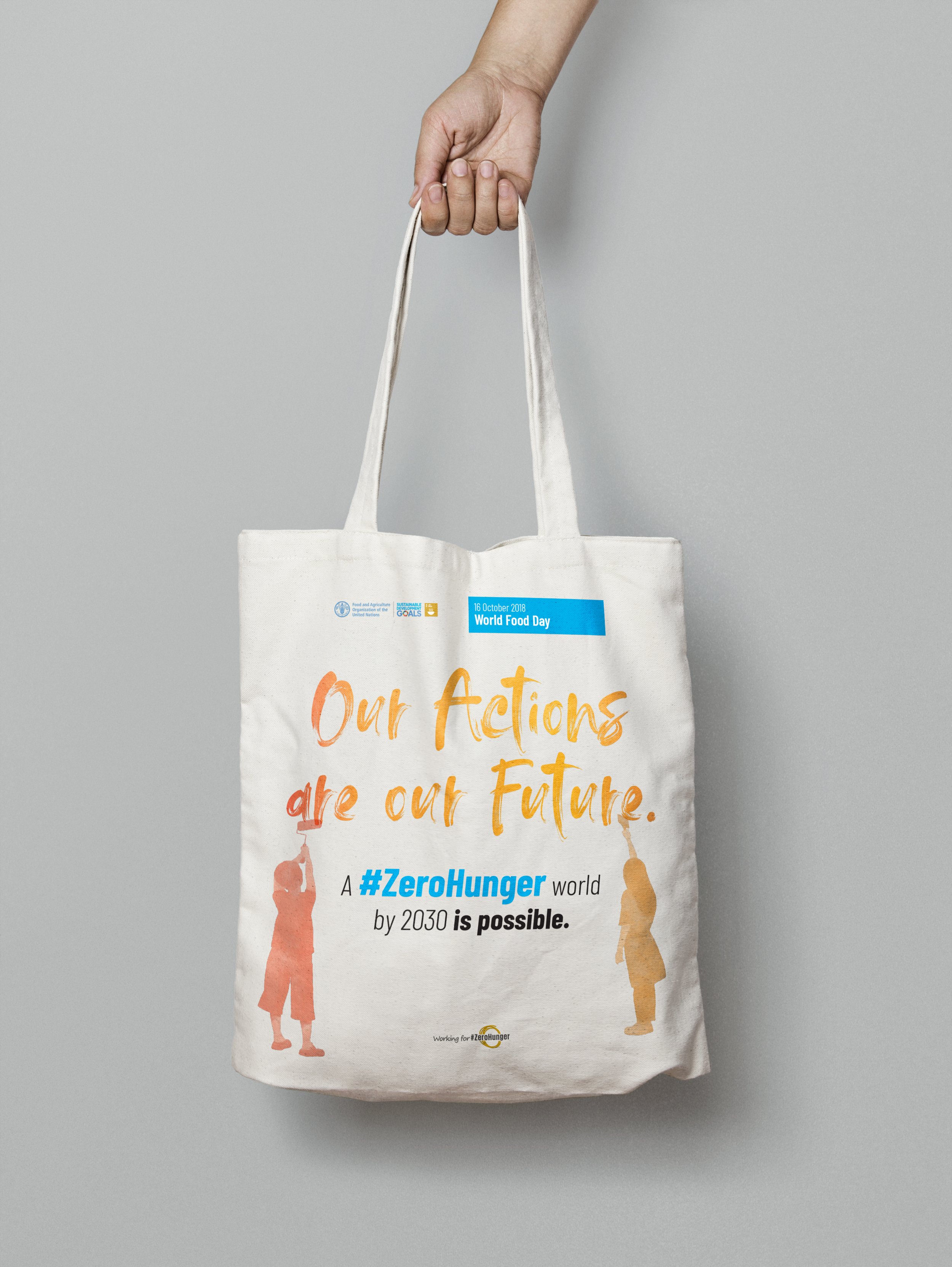 White tote bag with orange and blue text promoting World Food Day, featuring silhouettes of two children reaching for food, with the message about achieving a zero hunger world by 2030.