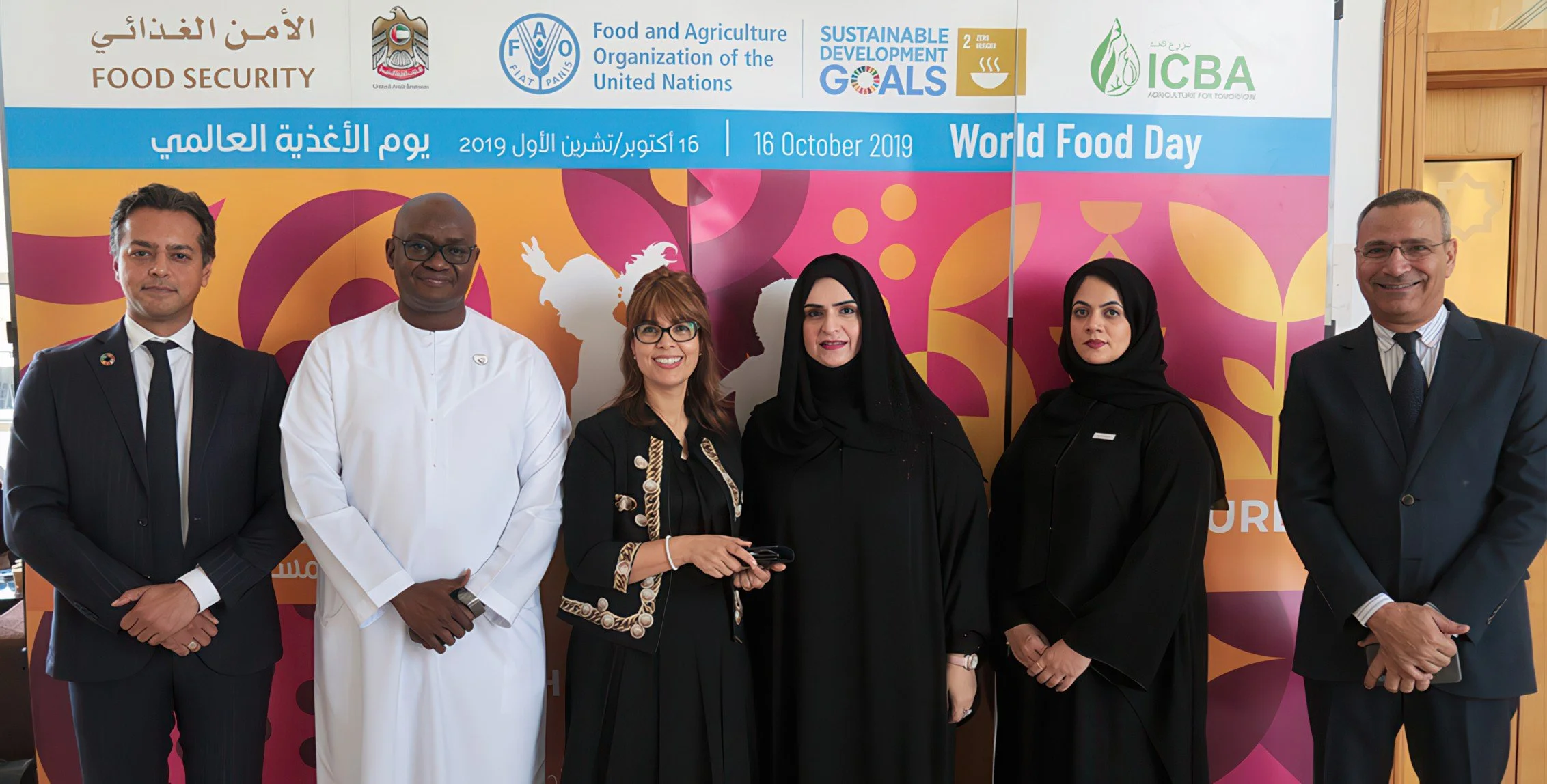 Group of six people standing in front of a World Food Day policy banner, including officials and a chef, celebrating October 16, 2019, with logos of FAO, UN, and other organizations.