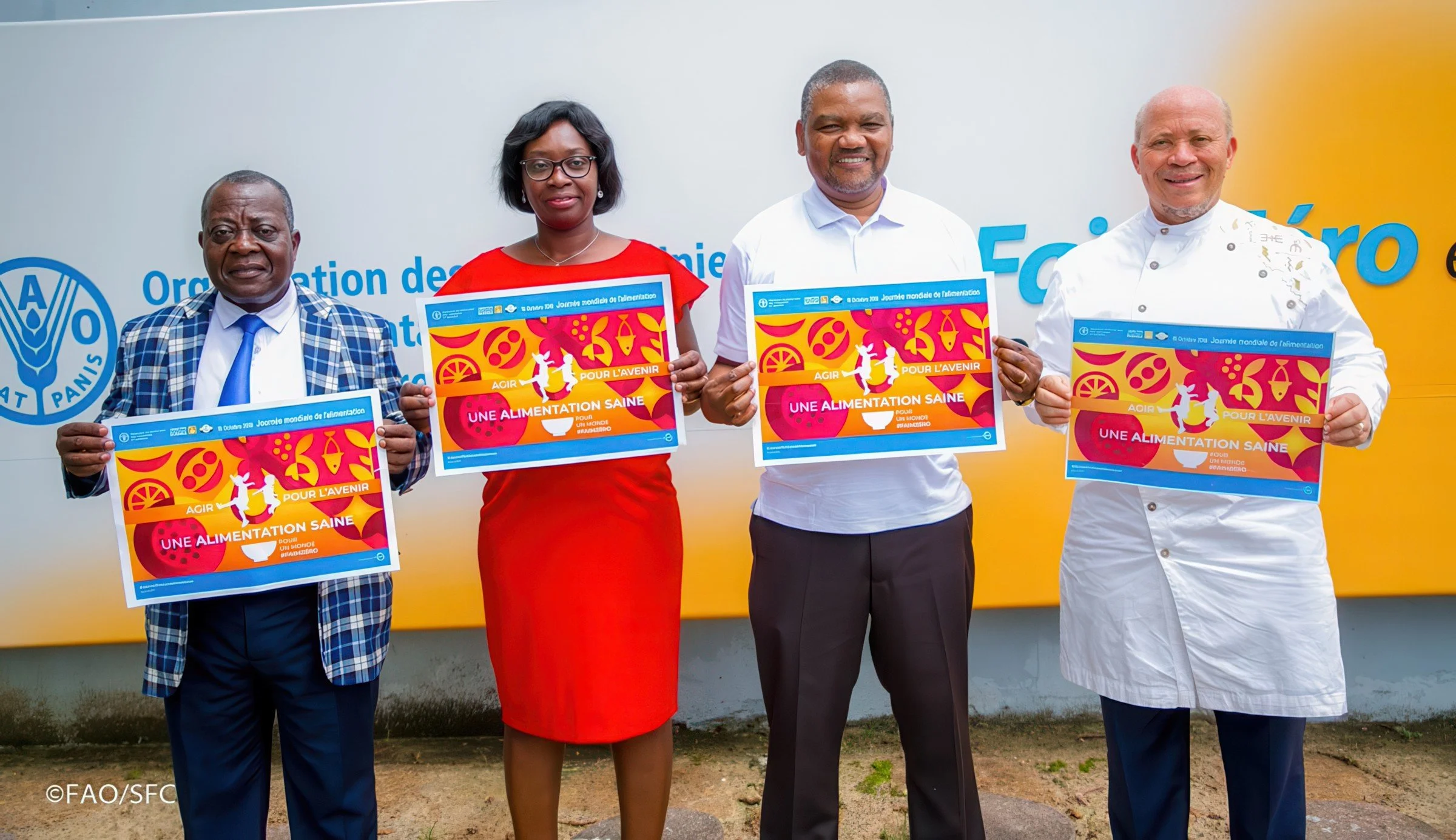 Four people standing outdoors holding posters promoting healthy eating, with a logo and French text on the posters.