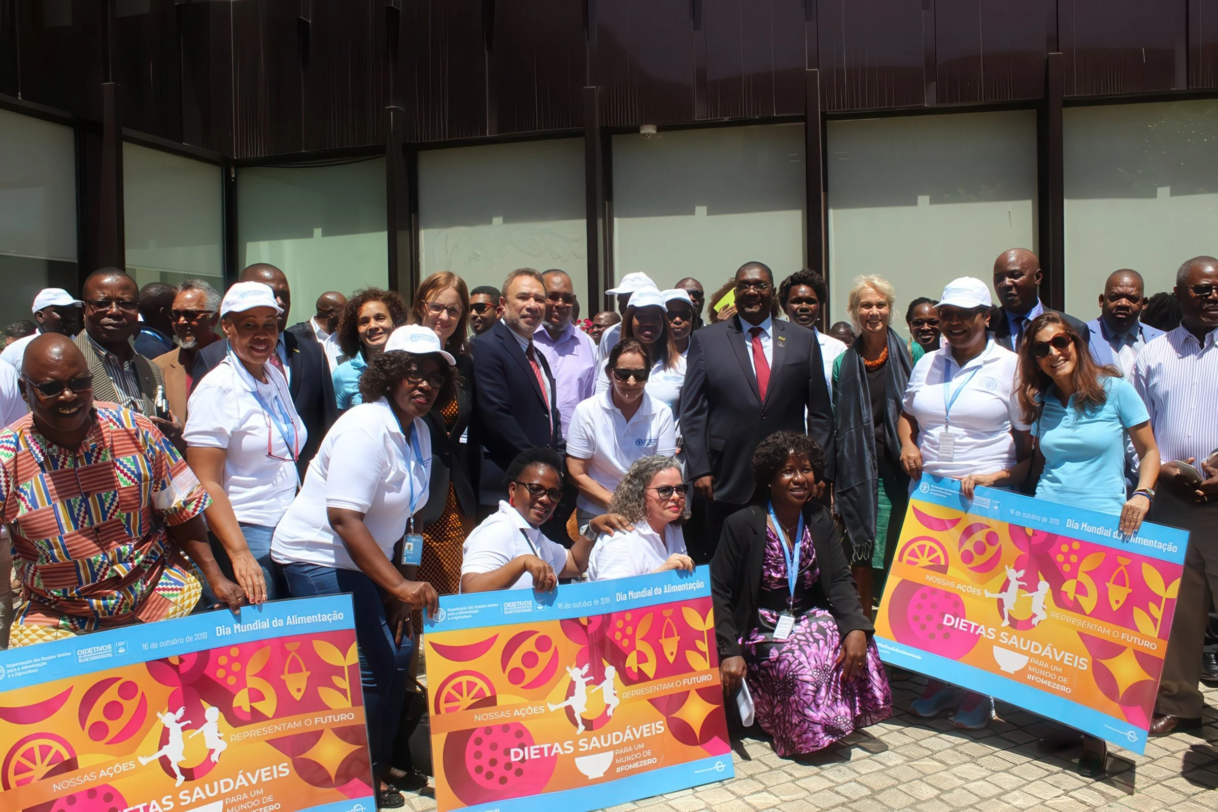 A diverse group of people gathered outdoors for an event, holding colorful signs promoting healthy diets for a better future, with some posing for the camera.
