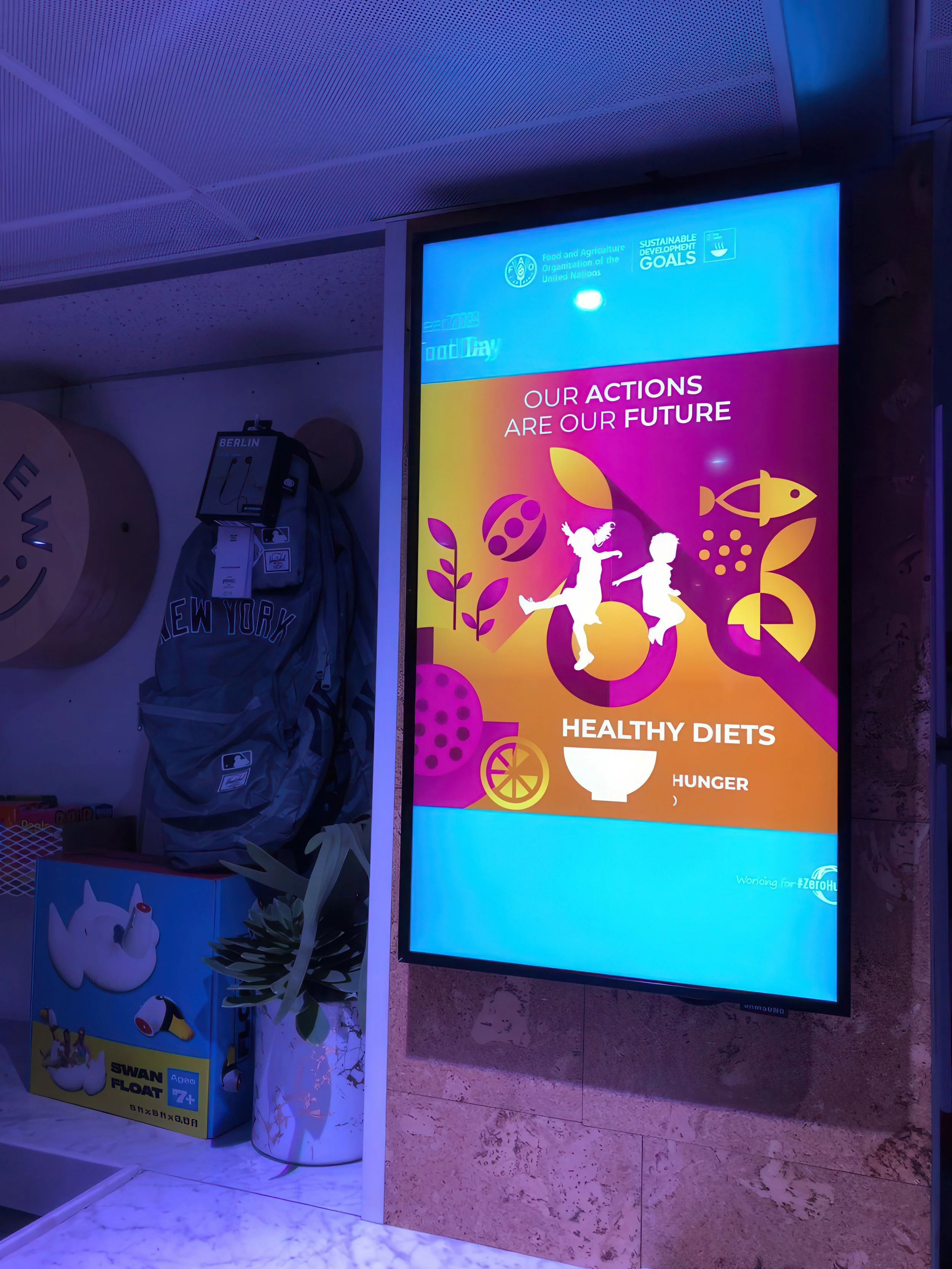 Digital display promoting actions for a sustainable future, featuring children and symbols of healthy diets, the environment, and food. There is a section mentioning the United Nations Food and Agriculture Organization and the Sustainable Development
