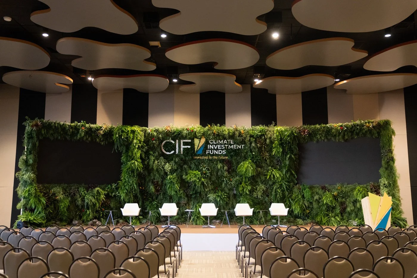 A conference stage with a green plant wall backdrop and the CIF Climate Investment Funds logo, set up with chairs and microphones for a panel discussion.