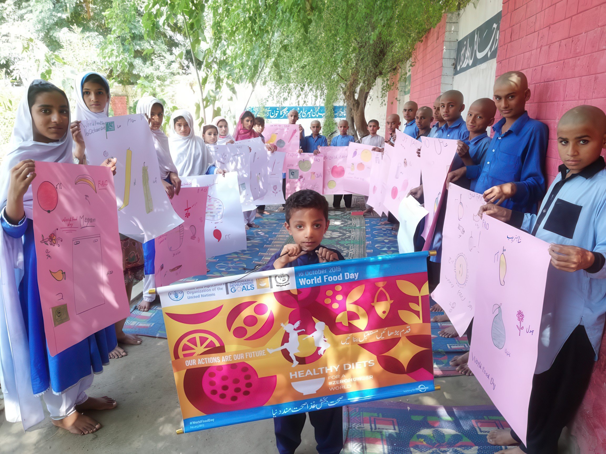 School children and students holding colorful posters and banners for World Food Day celebration outdoors under trees.