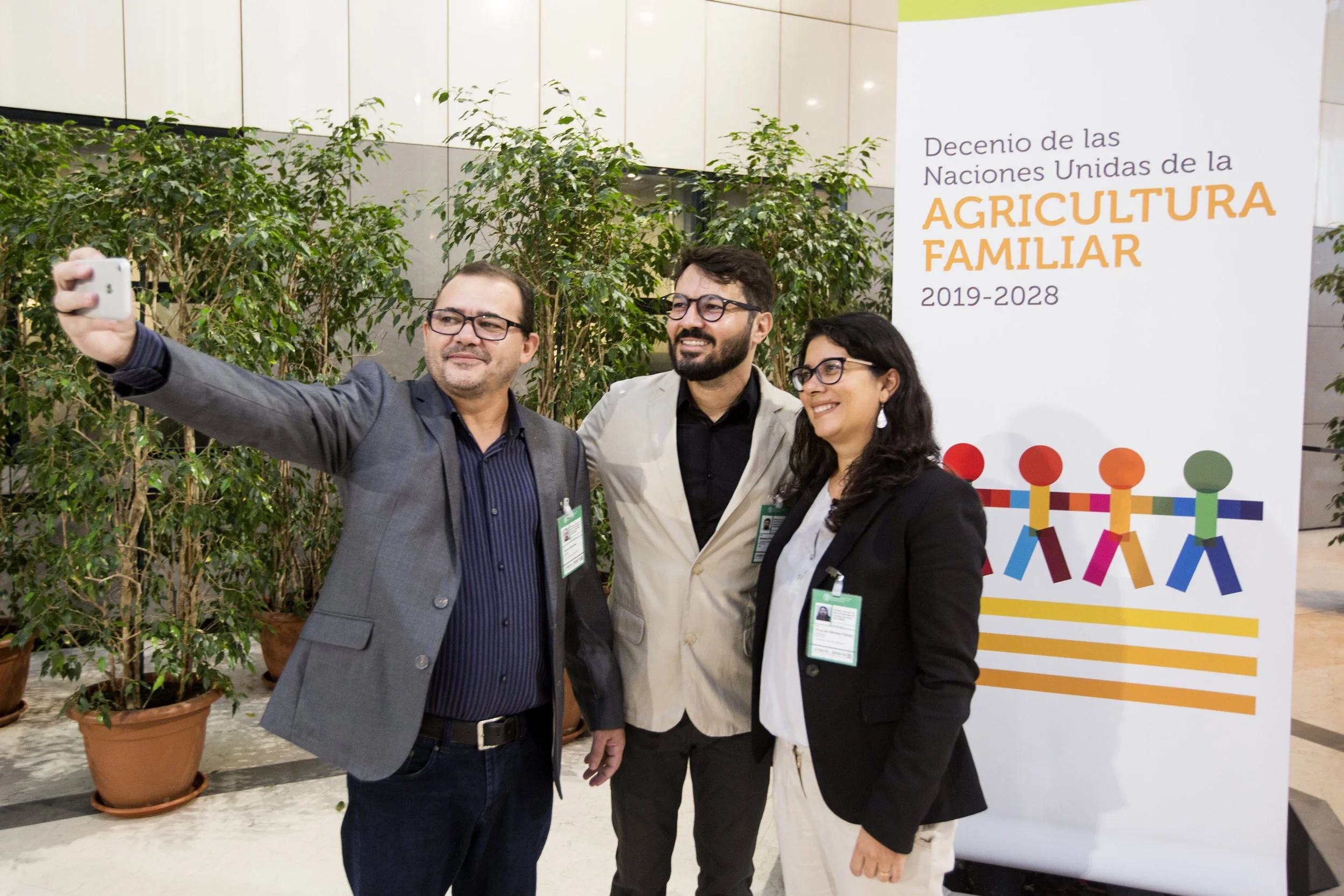 Three people taking a selfie at an event, standing in front of a sign that mentions the United Nations Decade of Family Farming 2019-2028.