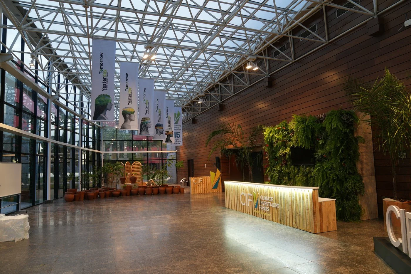 Indoor conference center with high glass ceiling, potted plants along the left, and a wooden reception desk with logo for Climate Investment Funds on the right.